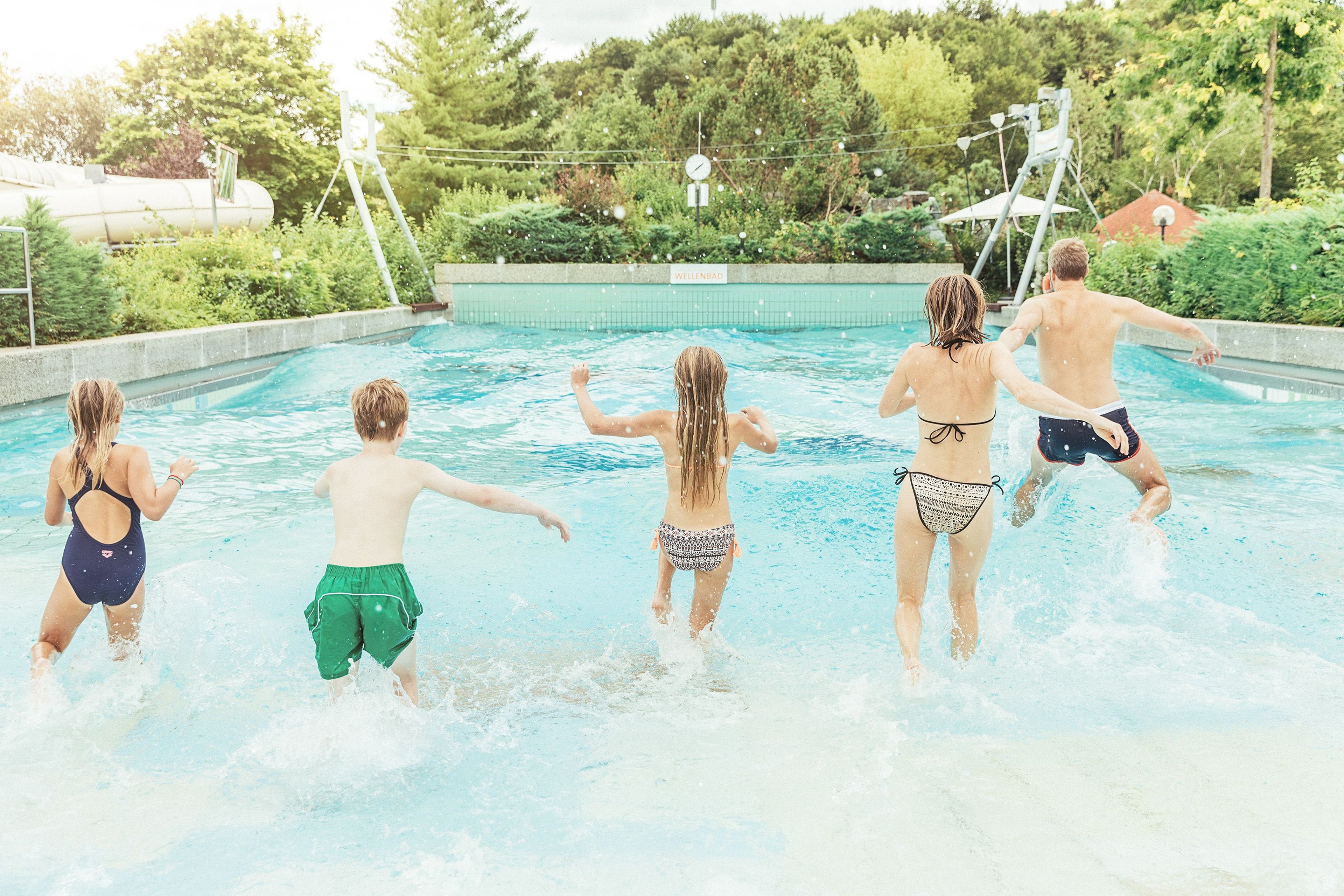 Family runs into the water in the wave pool in the outdoor area.