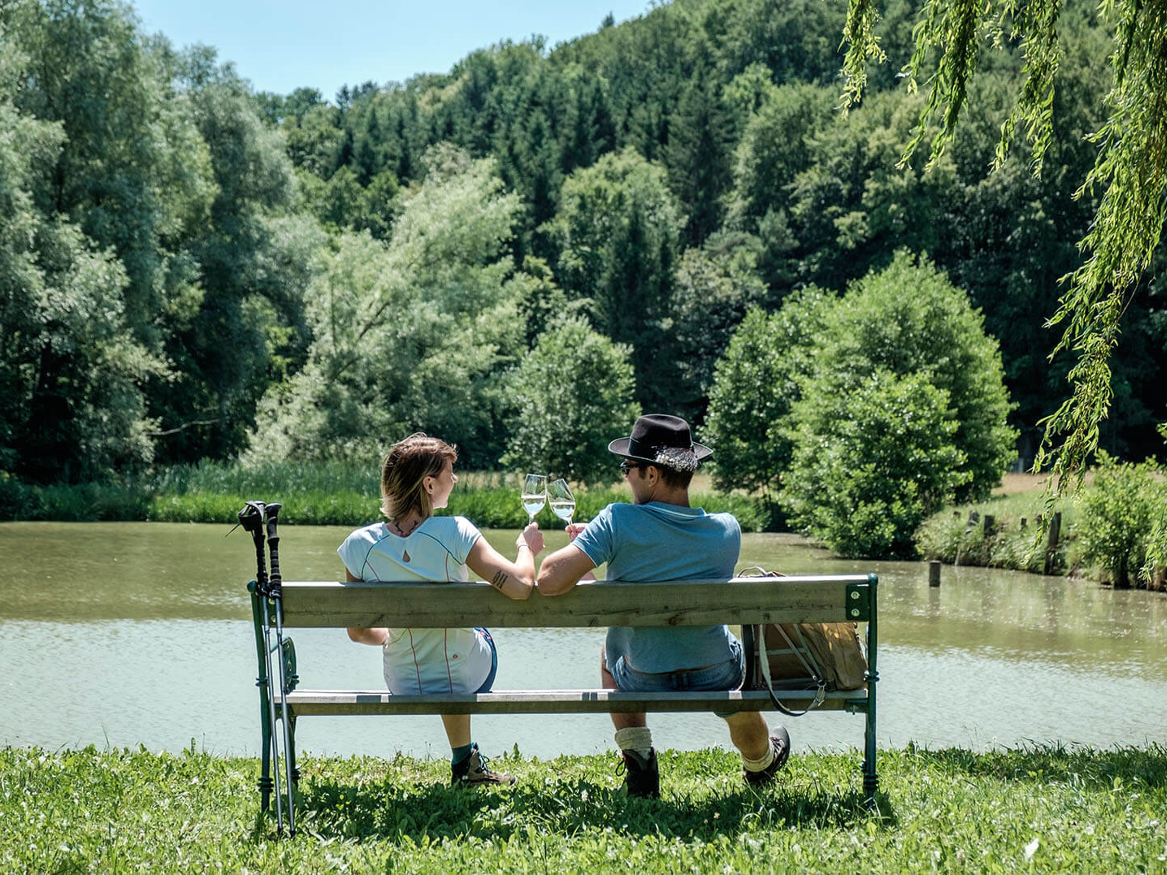 Ein Paar trinkt Wein am Teich bei Sonnenschein.