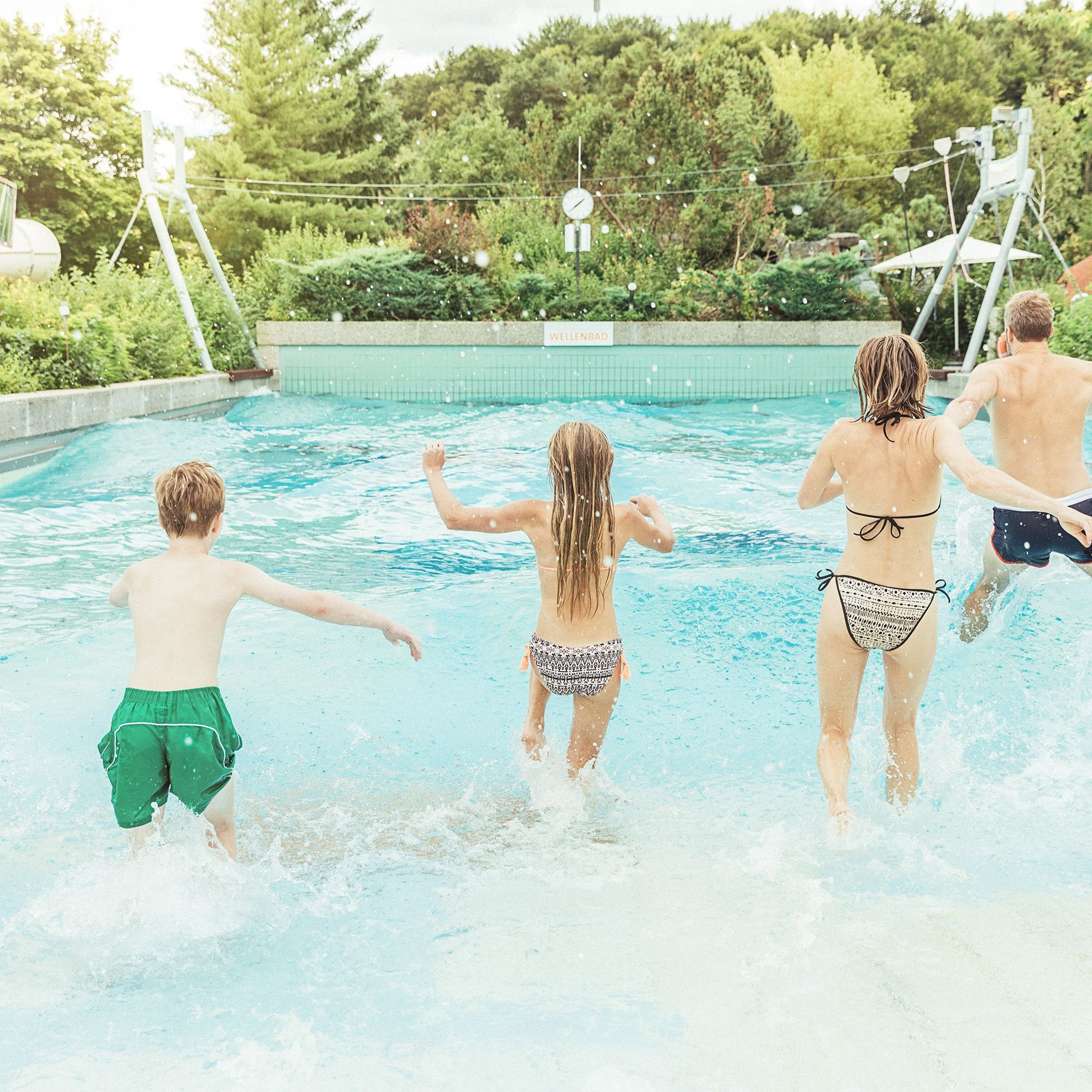 Familie läuft ibeim Wellenbad im Freibereich ins Wasser.