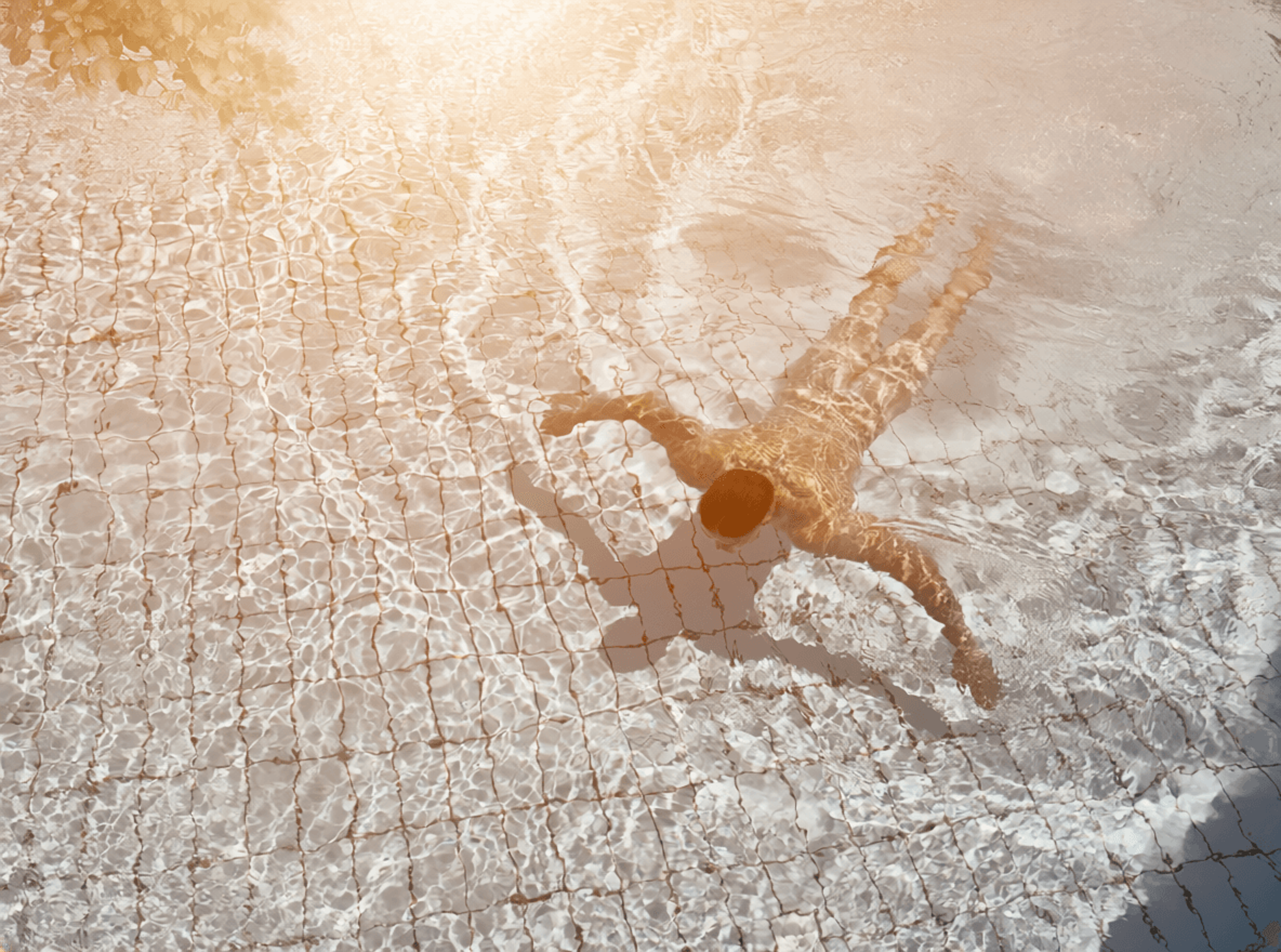 Man swimming on his front with outstretched arms in a pool with a visible tile pattern
