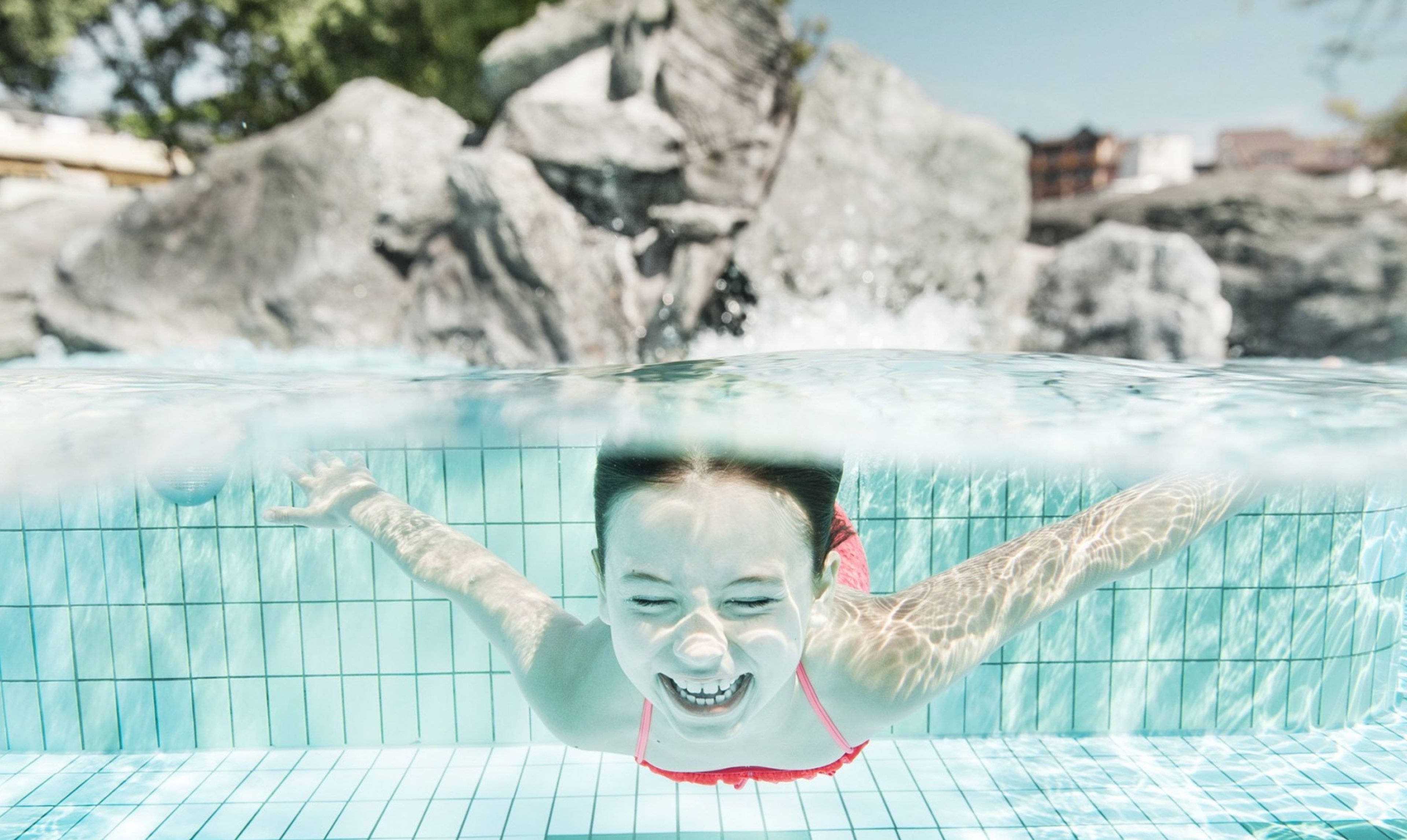 A child dives into the outdoor pool at Therme Loipersdorf and laughs.