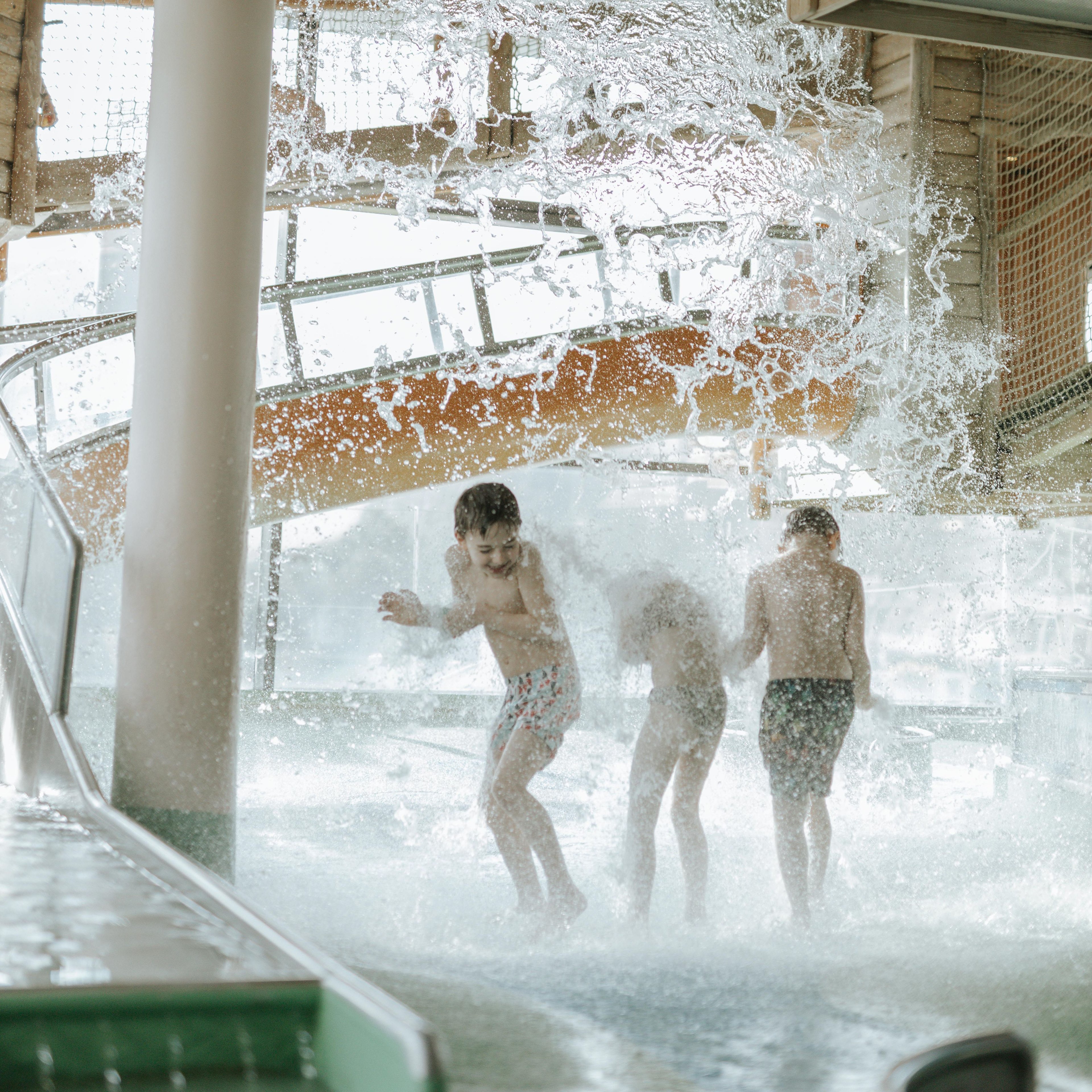 Kinder im Wasserspielpark die von der Kürbisdusche von oben Nass gemacht werden.