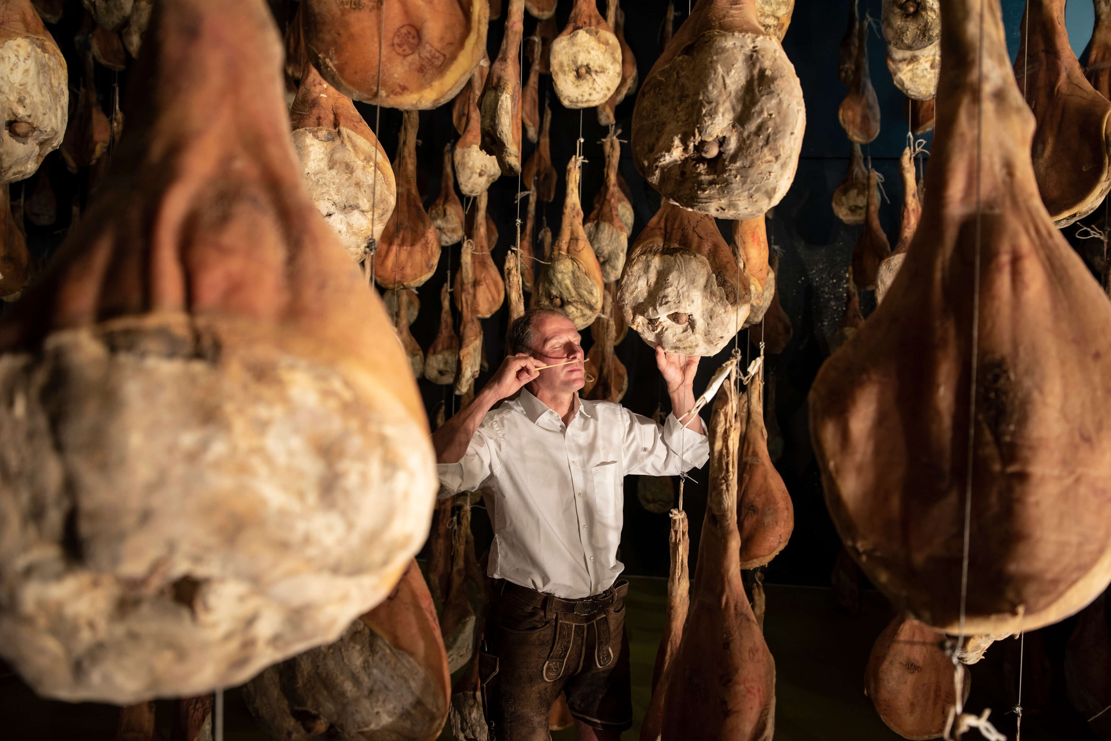 Die Räucherkammer voller Schinken und einem Mann am Bild.