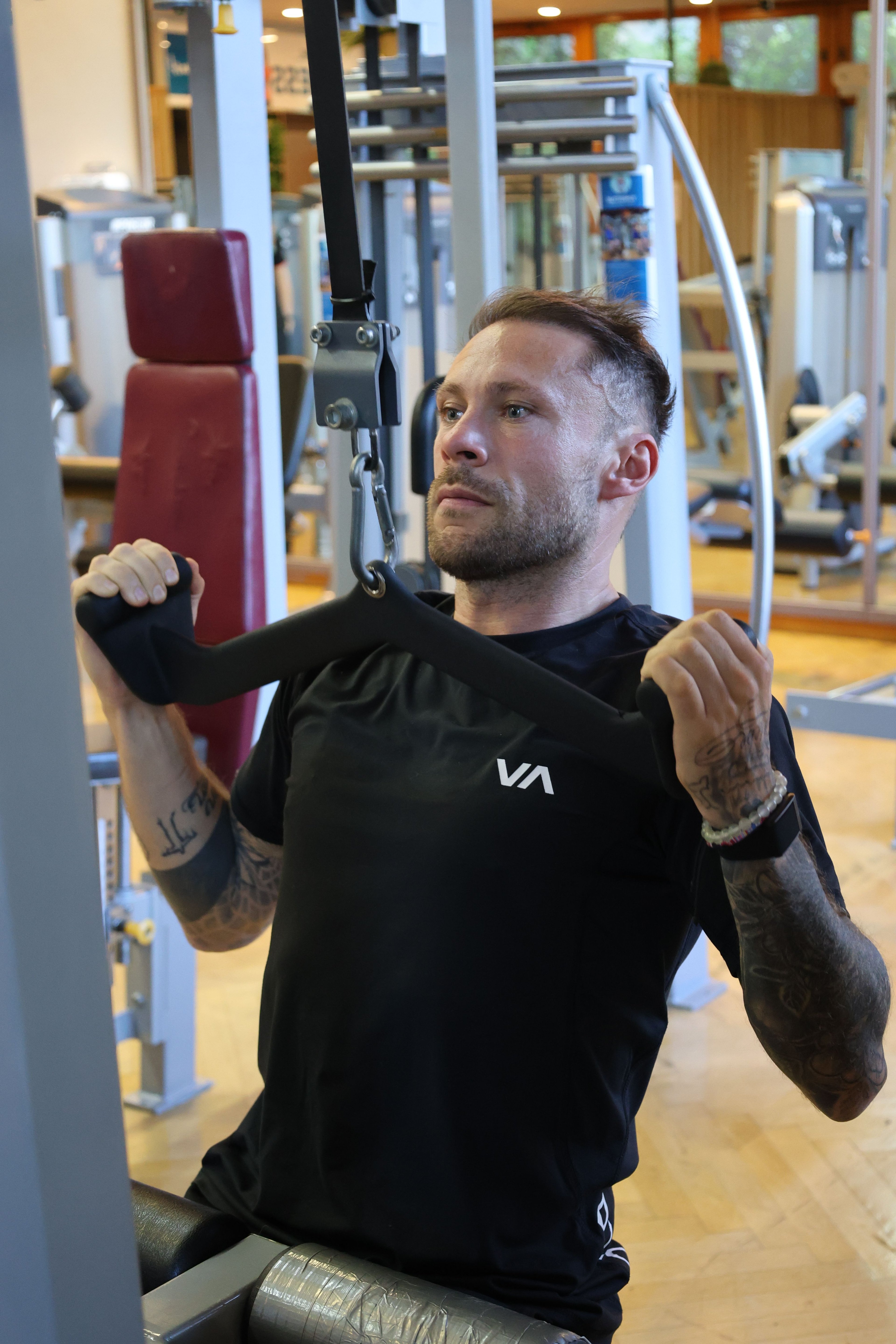 Mann sitzt an Fitnessgerät und führt Übung mit abgewinkelten Armen aus