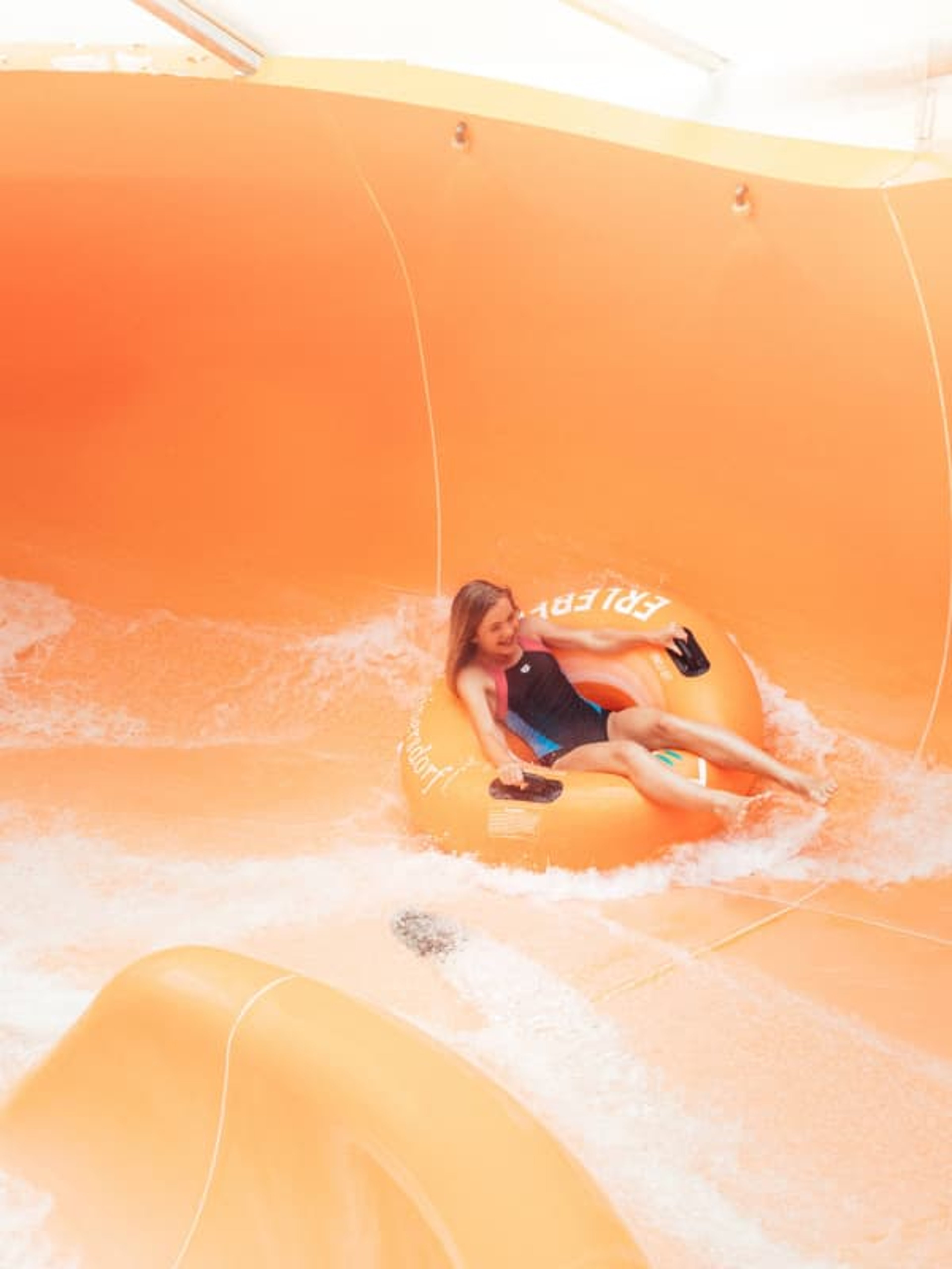 A child in a tire slides down a water slide.