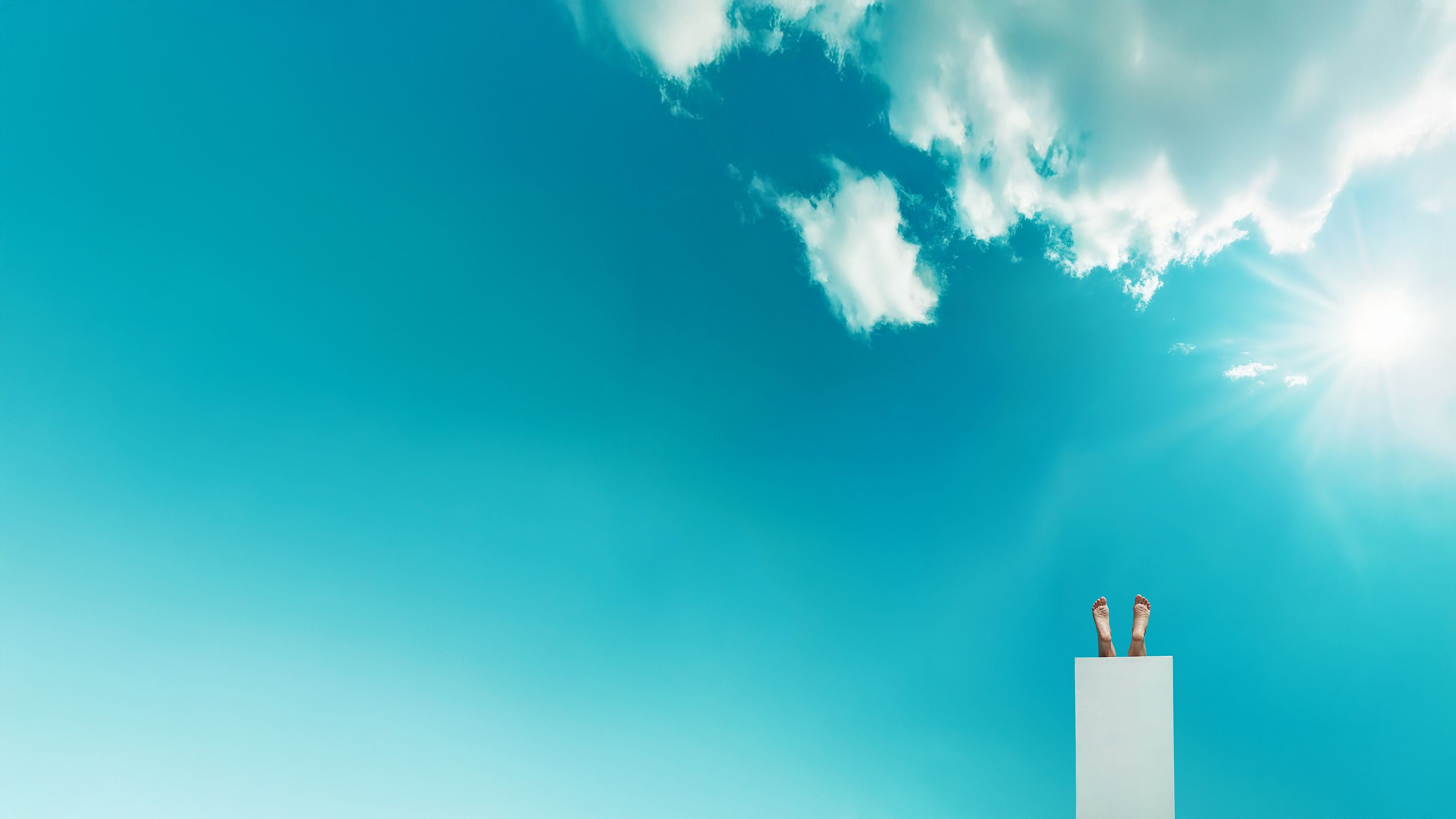 View of the sky with clouds in the foreground a diving board with feet.