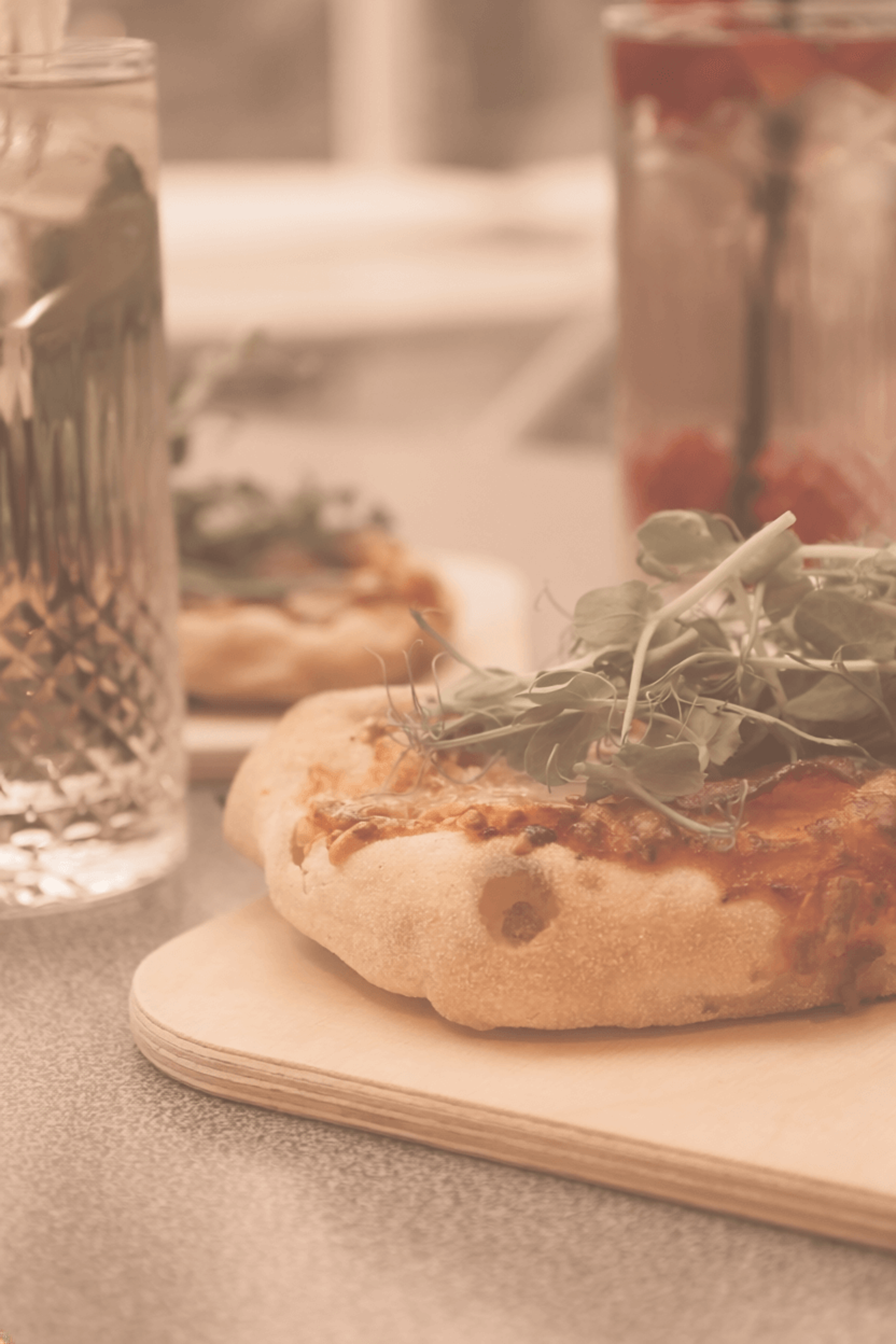 Pizza with fresh arugula on a wooden board, next to a glass of water and a drink with a straw