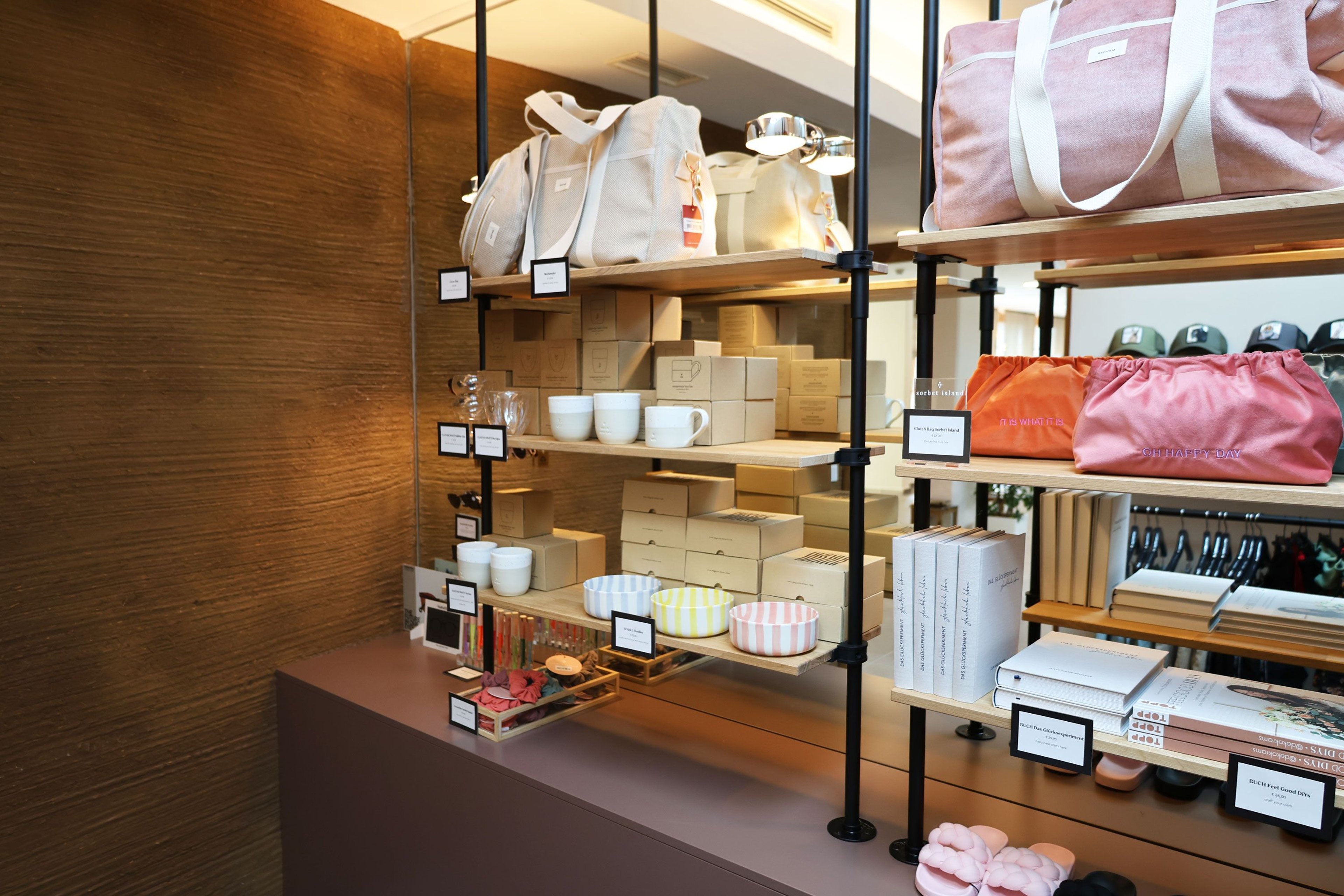 Shelf with white and pink bags, striped bowls, white cups, and several white boxes in a store.