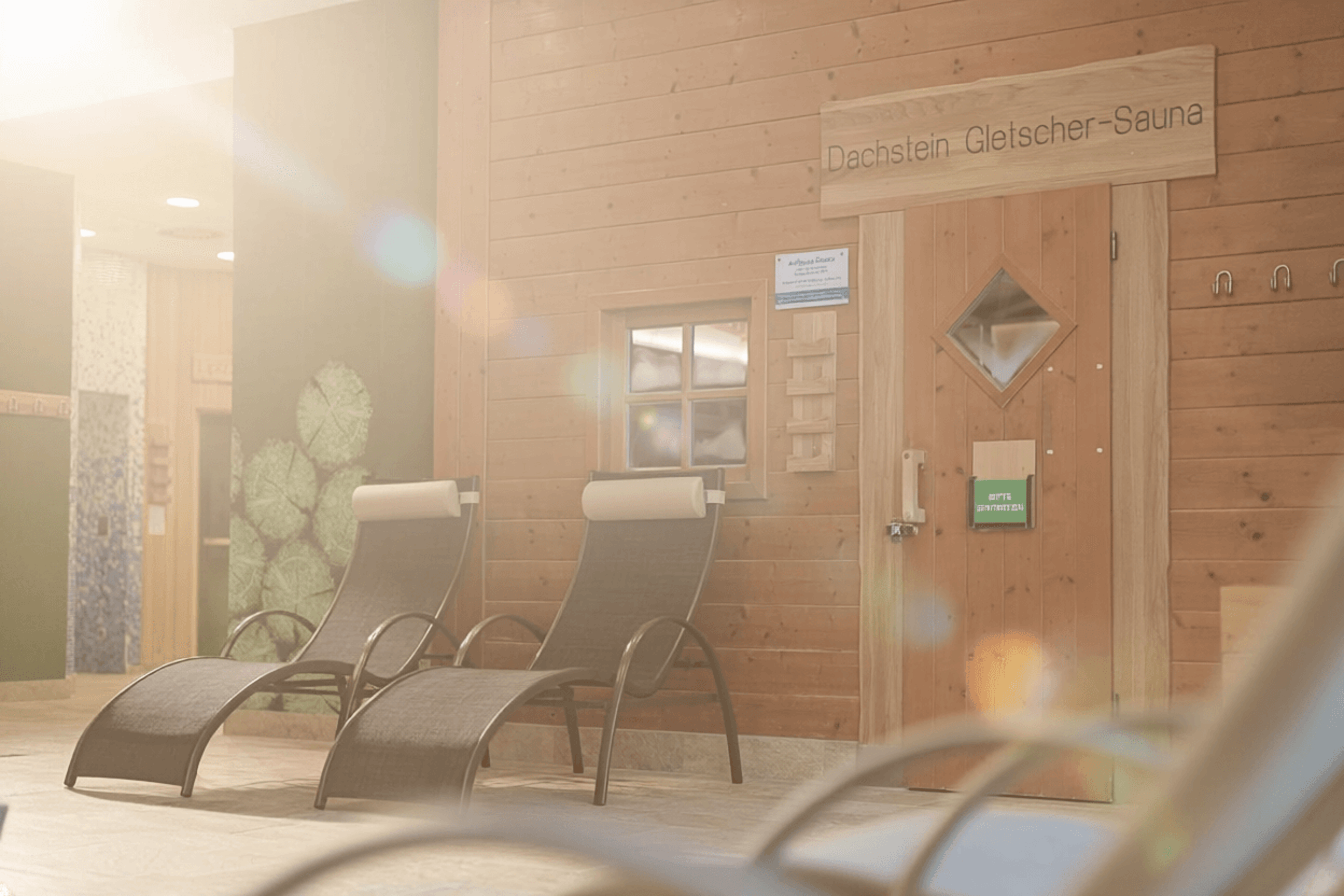 Interior with two loungers in front of a wooden wall and a door to the “Dachstein Glacier Sauna”