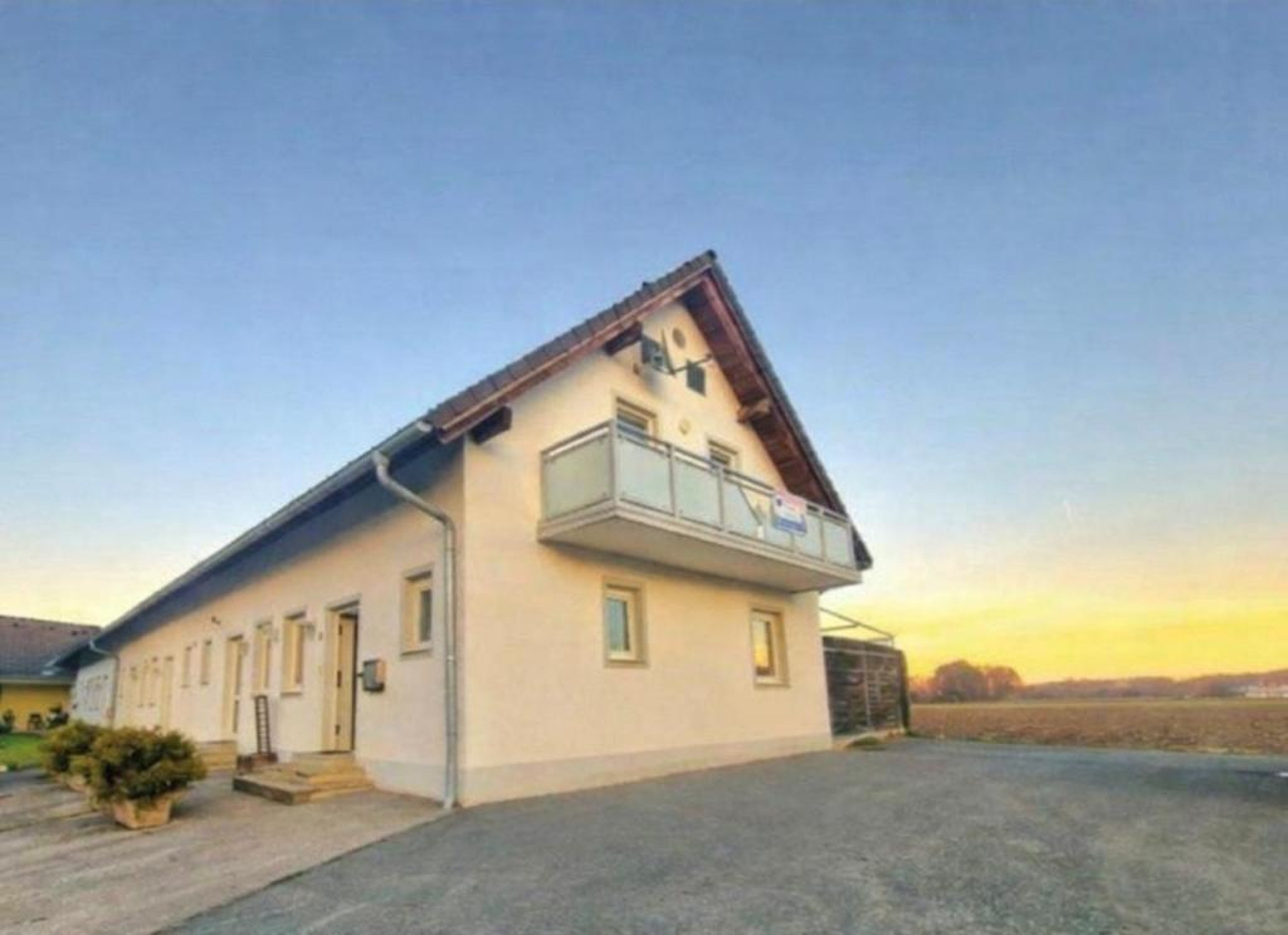 Single-family house with gable roof and balcony in front of open landscape at sunset