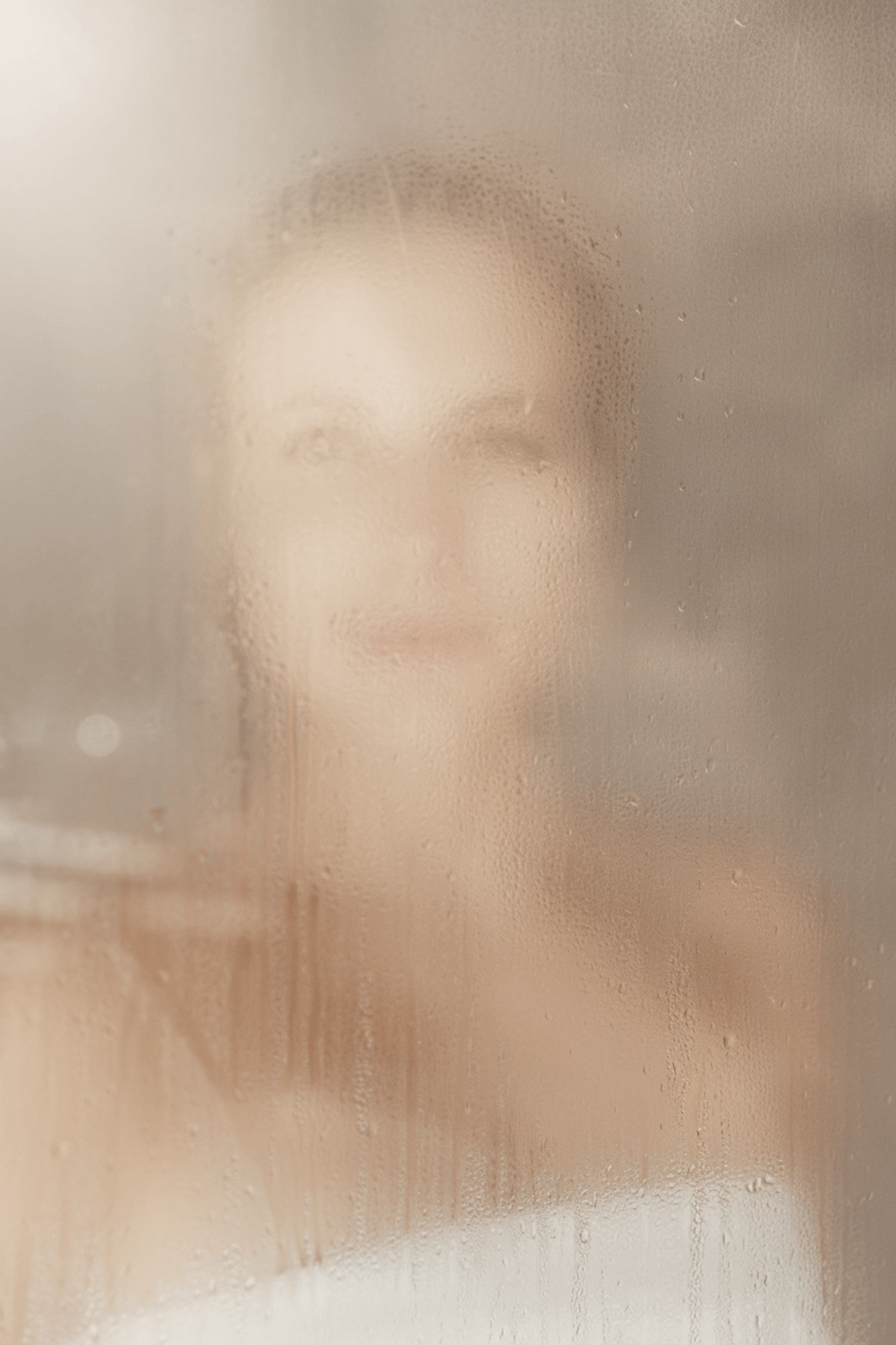 Verschwommene Silhouette einer Person hinter beschlagener Glasfläche mit Wassertropfen