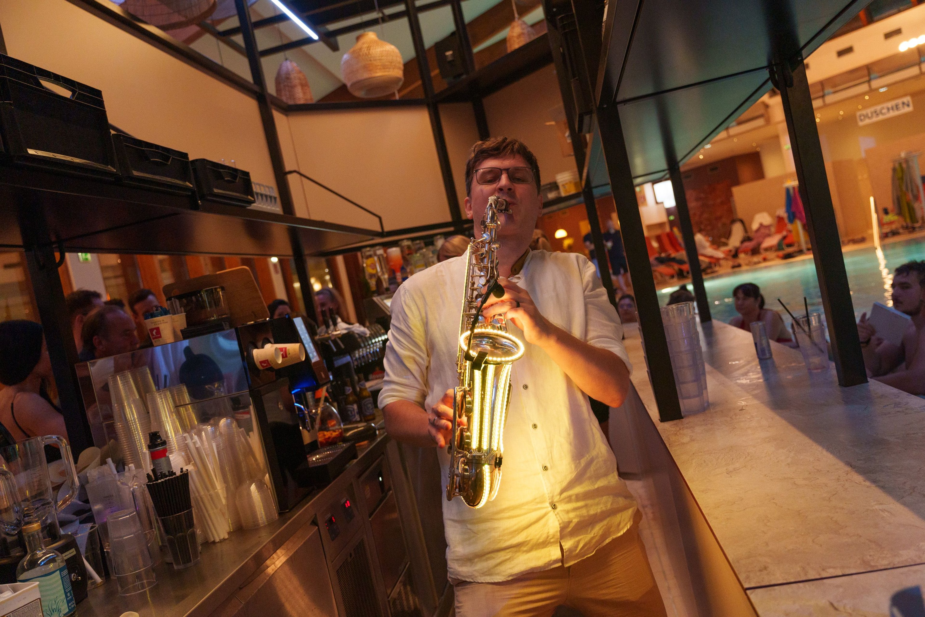 Person in white shirt playing saxophone with glowing green LED strips in dim indoor setting