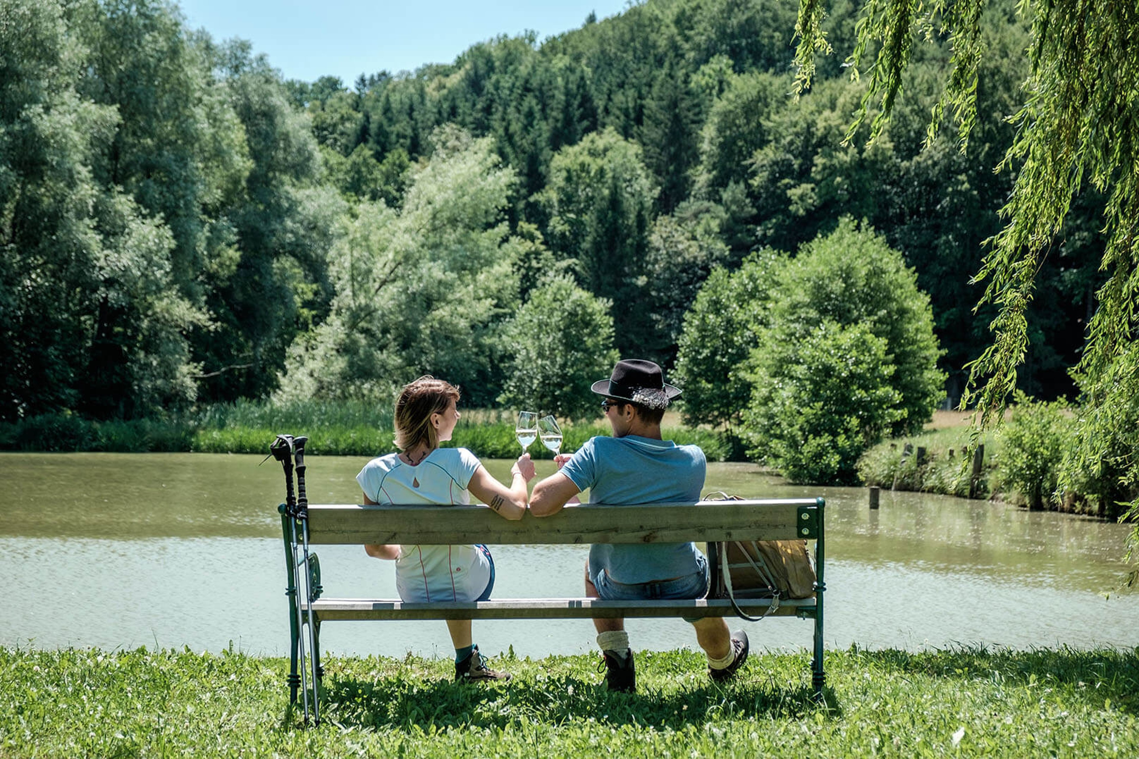 Ein Paar trinkt Wein am Teich bei Sonnenschein.
