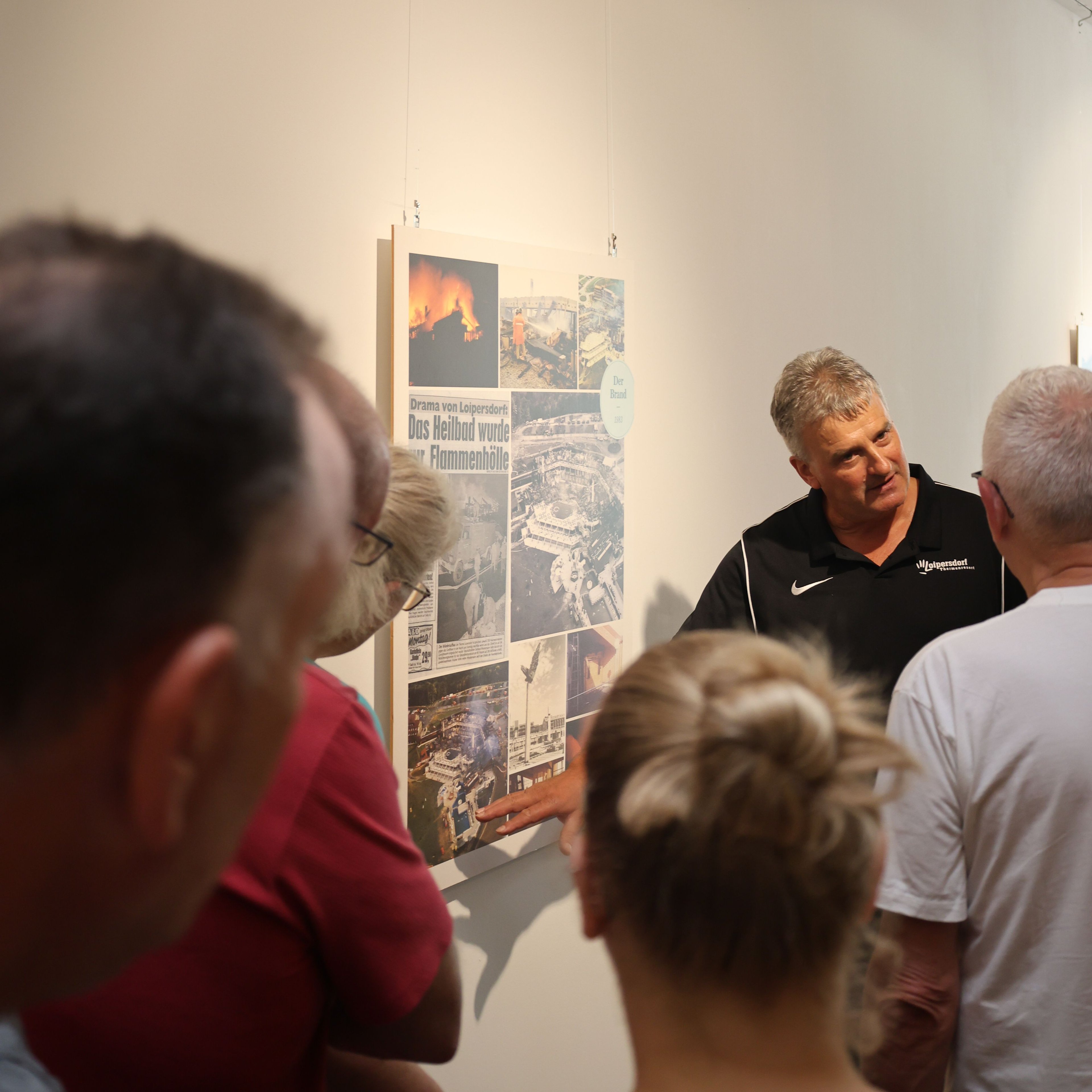 Several people stand in front of a wall displaying historical photos and newspaper clippings.