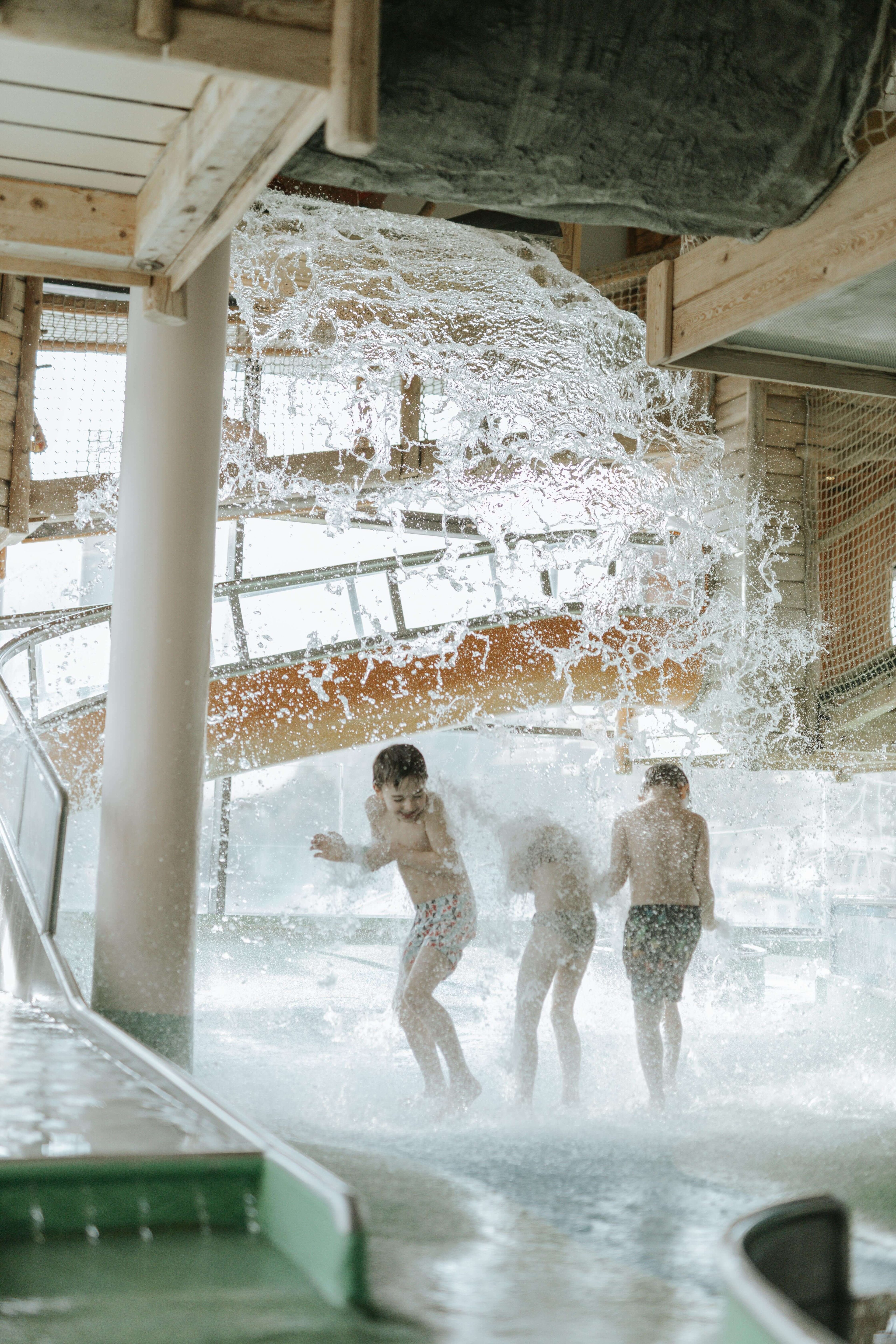 Children in the water play park getting wet from above by the pumpkin shower.