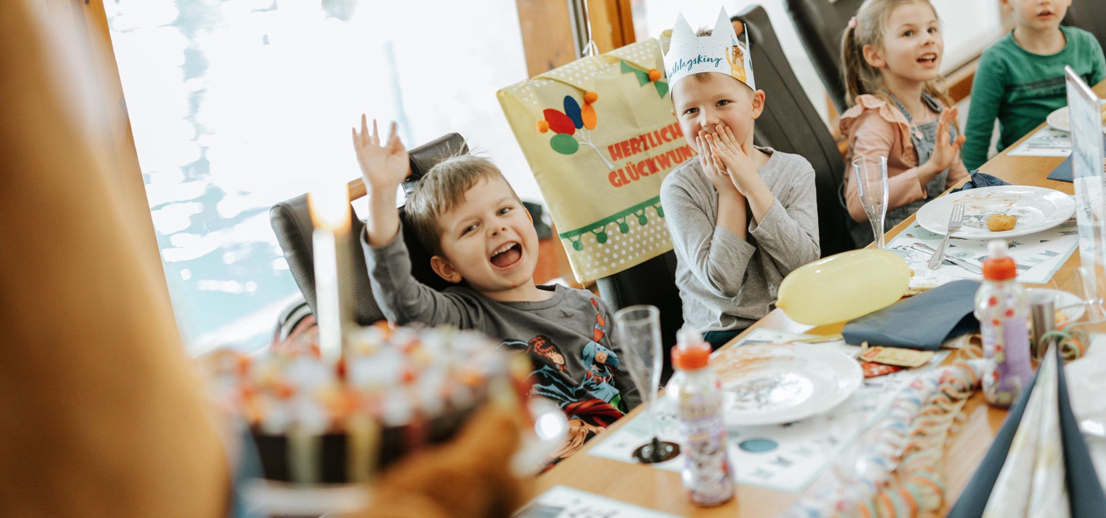Kinder sitzen am Tisch und freuen sich als die Torte serviert wird