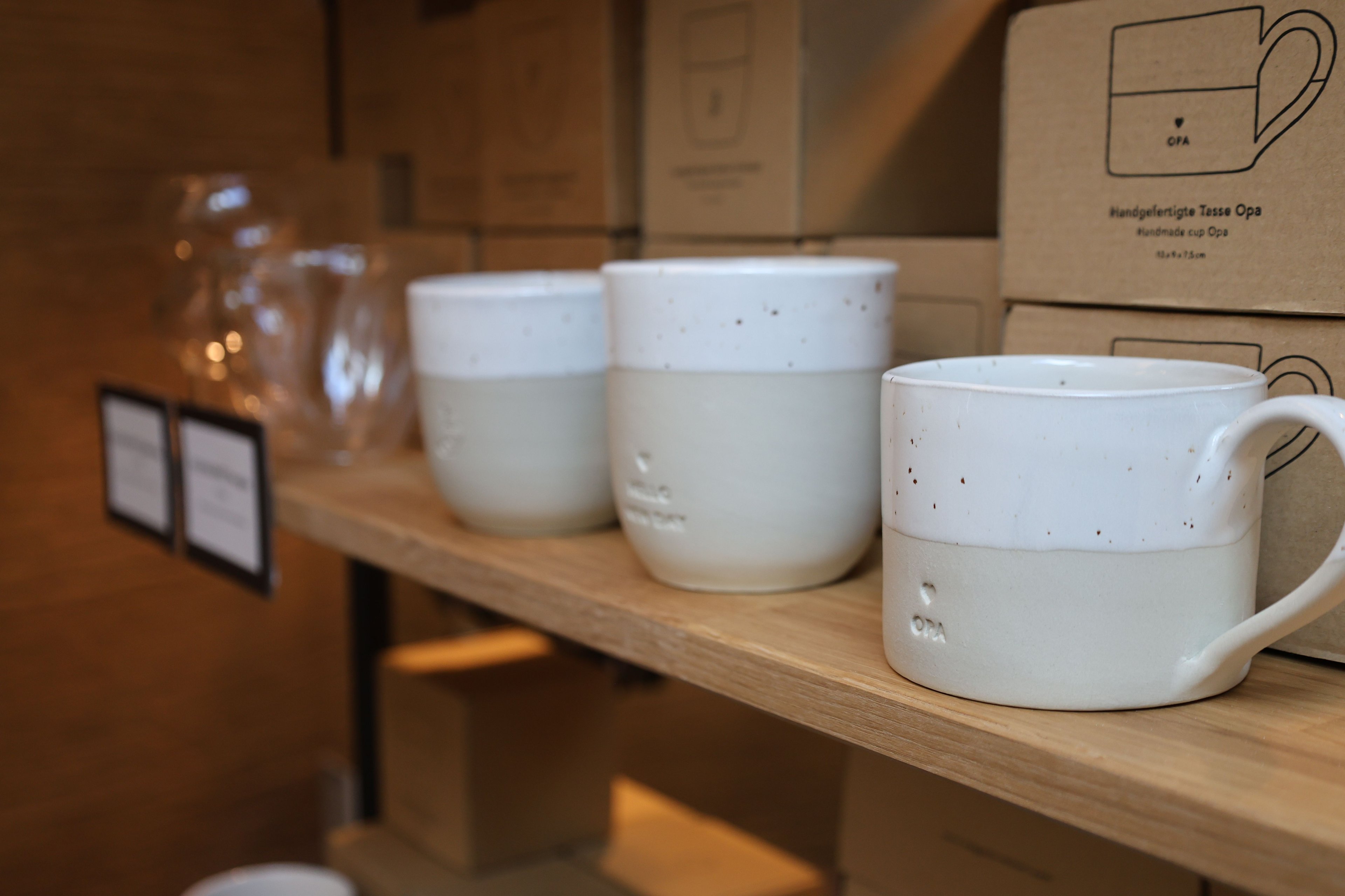 Three handmade cups in white with gray bases and fine black speckles stand on a wooden shelf.