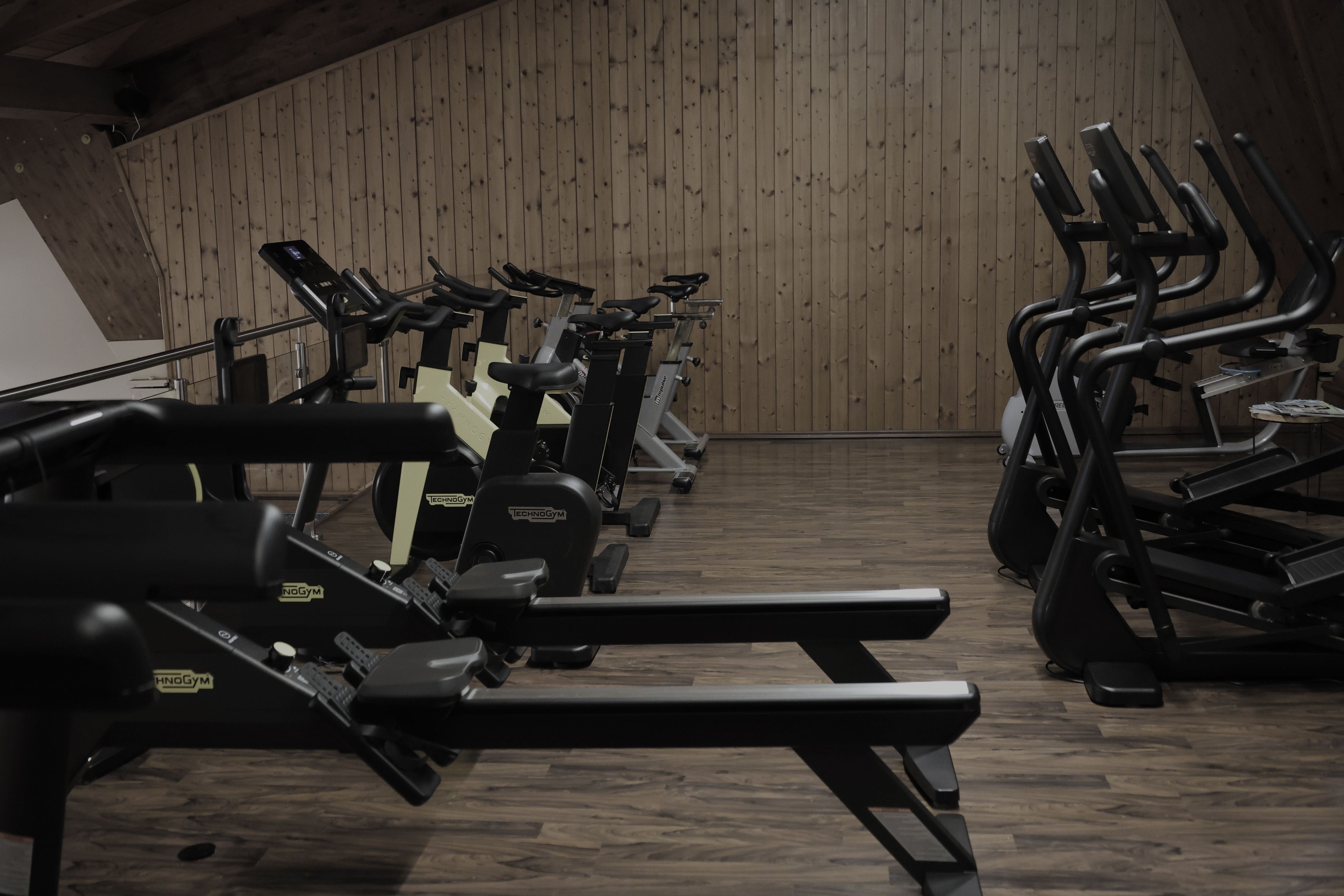 Interior of a gym with multiple rowing machines and stationary bikes in front of a wooden paneled wall