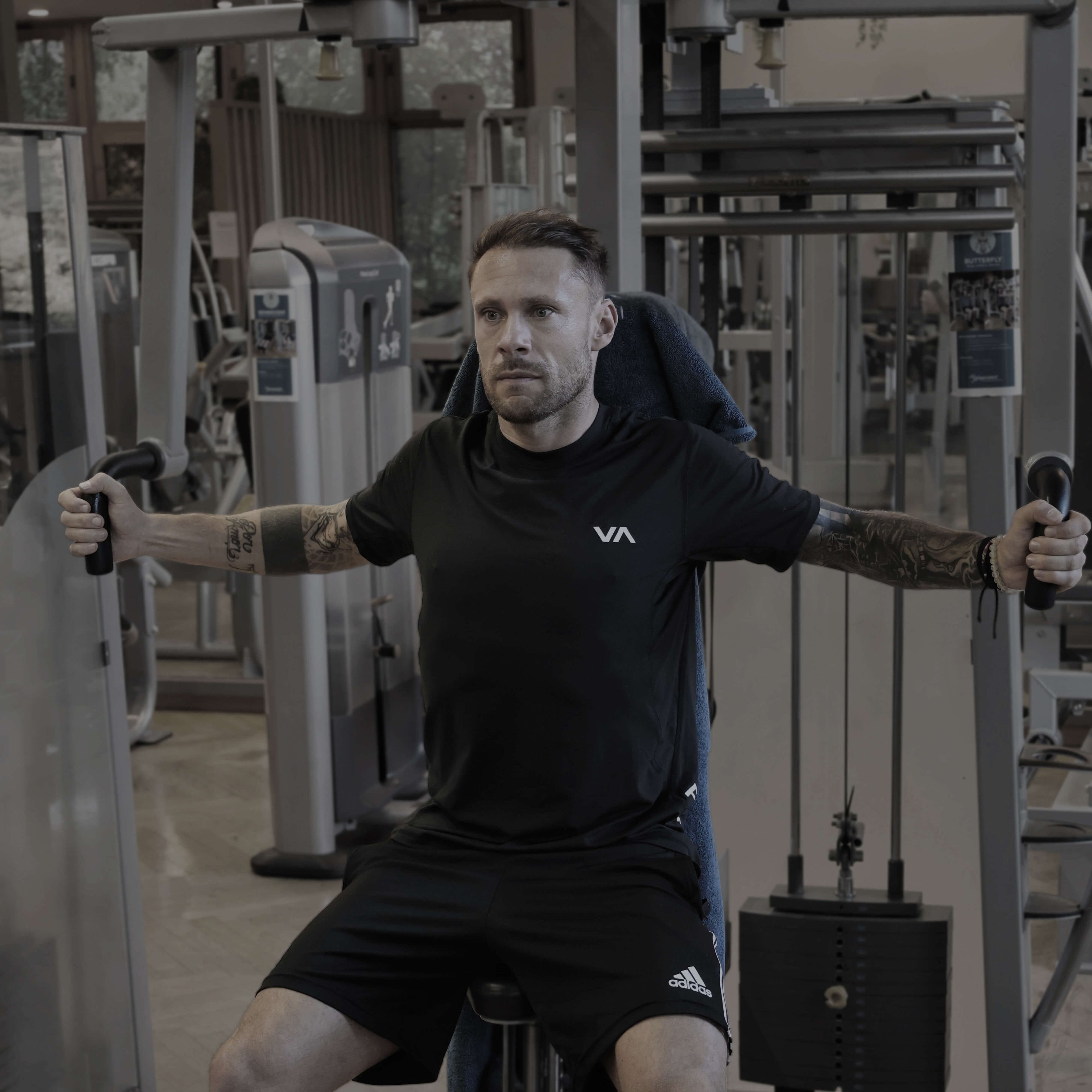 Mann sitzt an Fitnessgerät und führt Butterfly-Übung mit ausgestreckten Armen aus