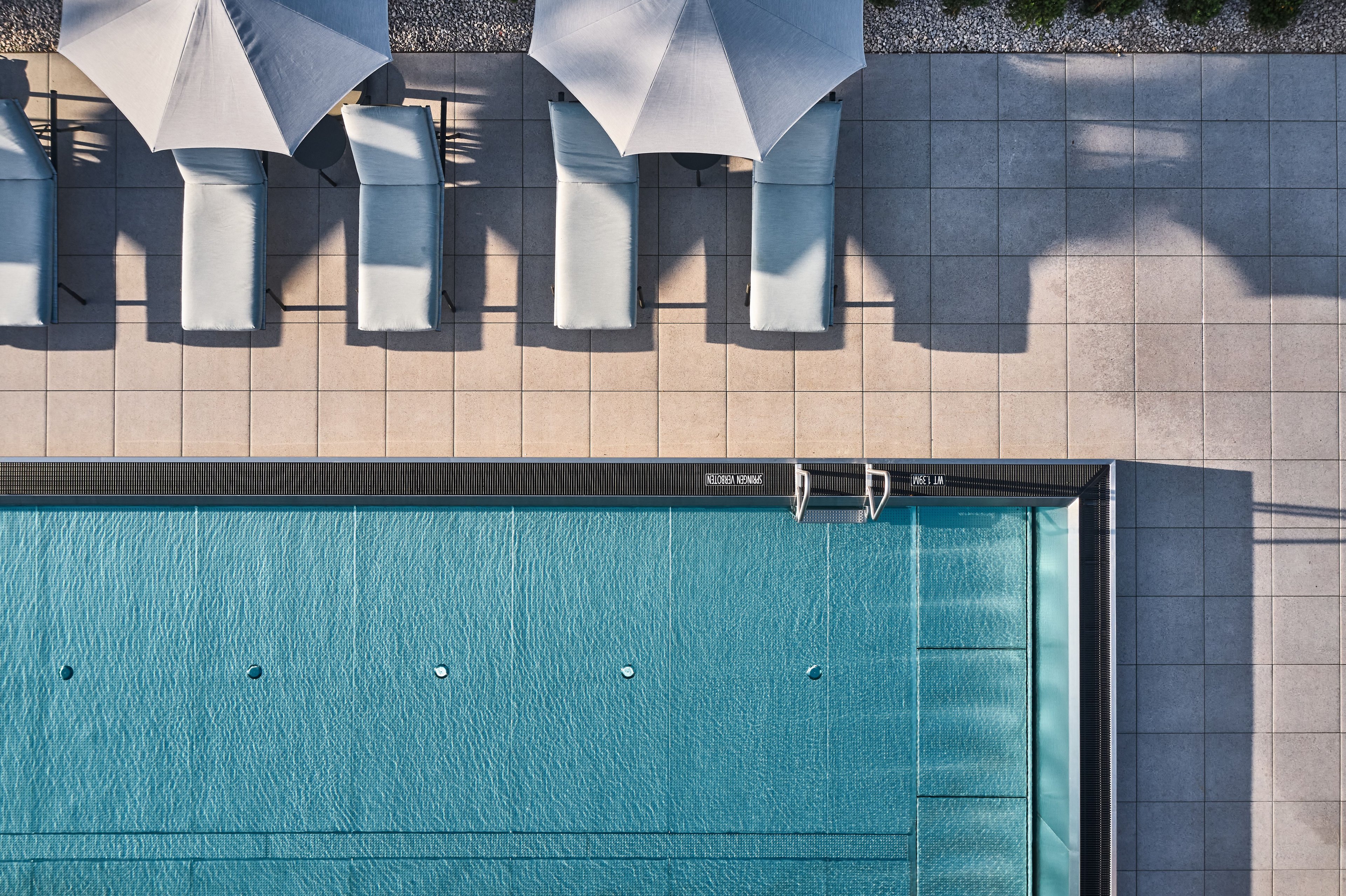 Luftaufnahme eines rechteckigen Schwimmbeckens mit Liegestühlen und Sonnenschirmen auf der Terrasse
