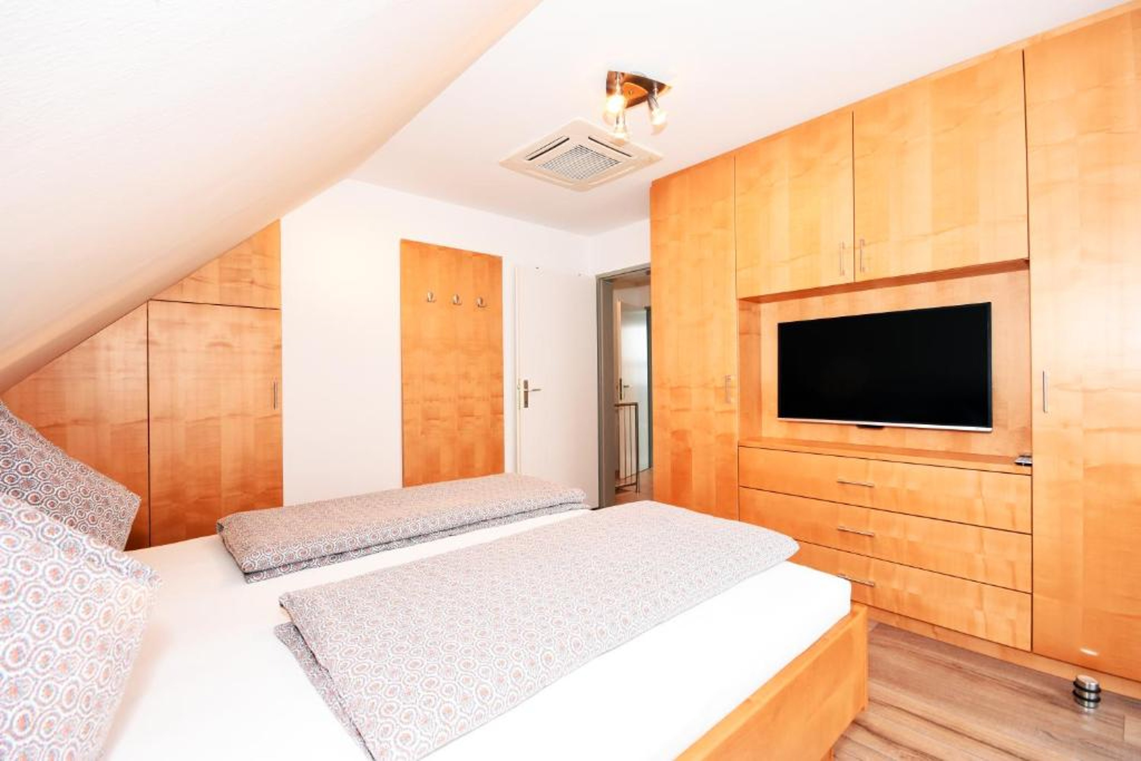 Bedroom with two single beds, built-in wardrobe, and wall-mounted TV under a slanted ceiling