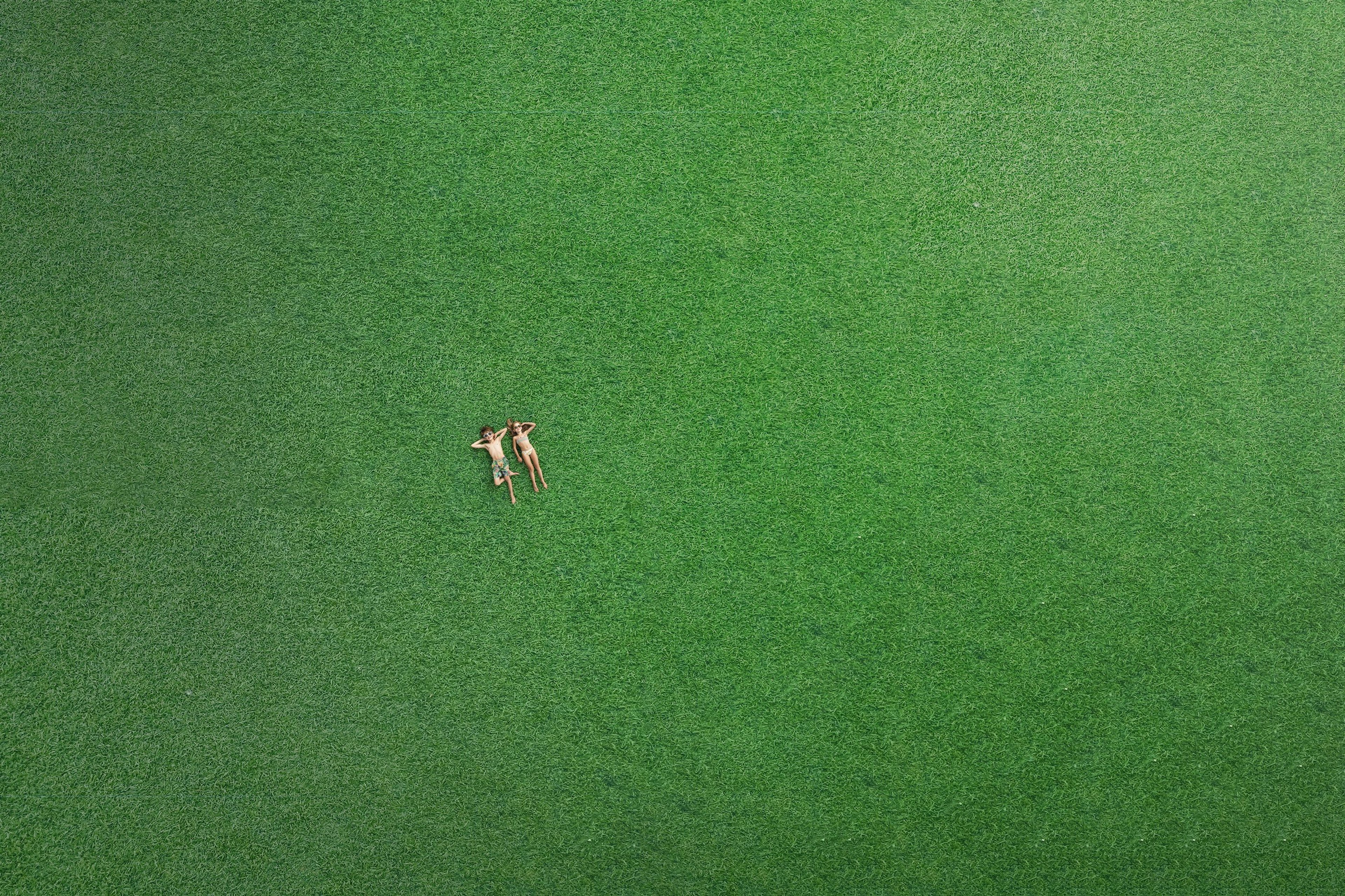 Rießige grüne Liegefläche im Freibereich und zwei Kinder die inder Wiese liegen. 
