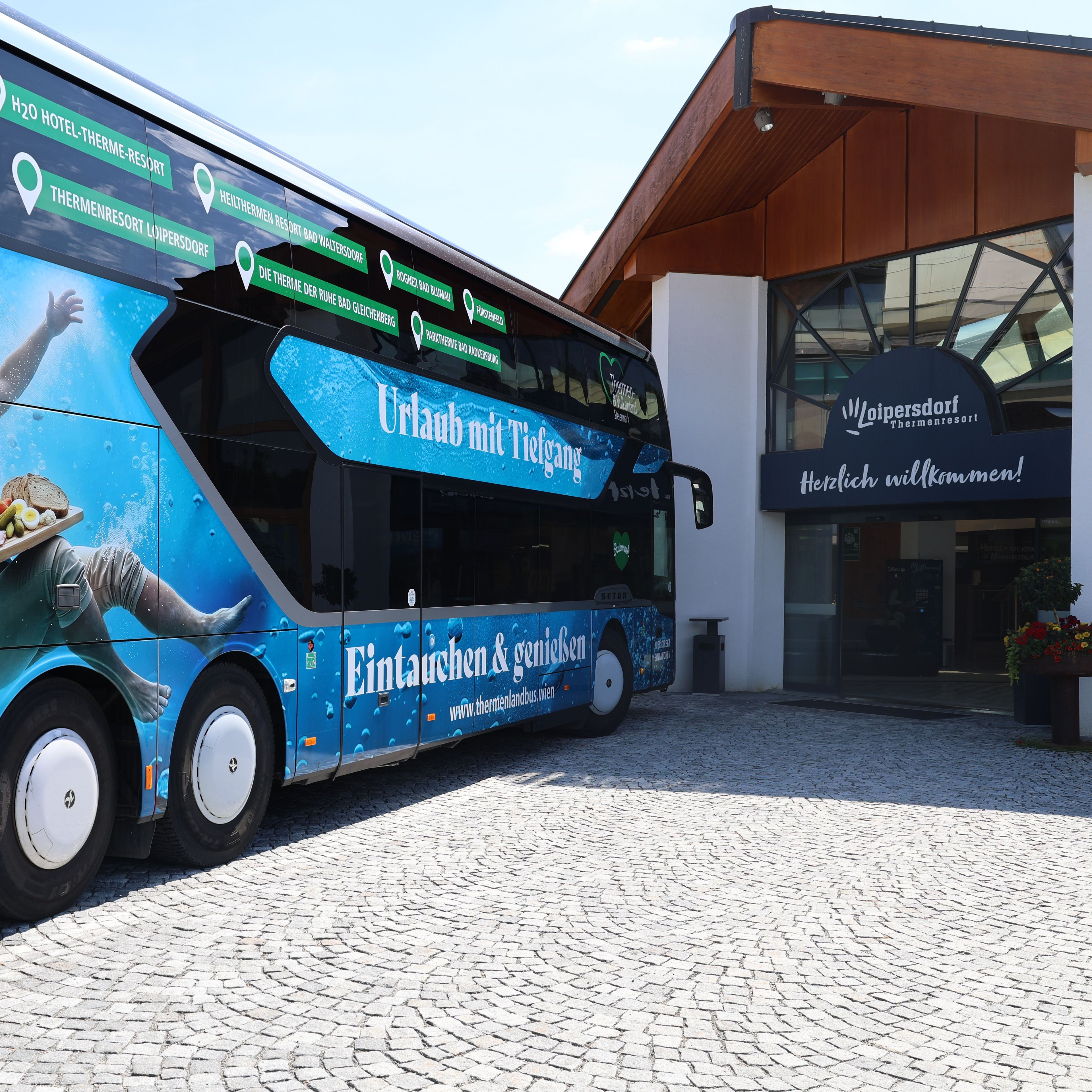 Tour bus with blue advertisement showing a person swimming underwater parked in front of a building entrance with planters