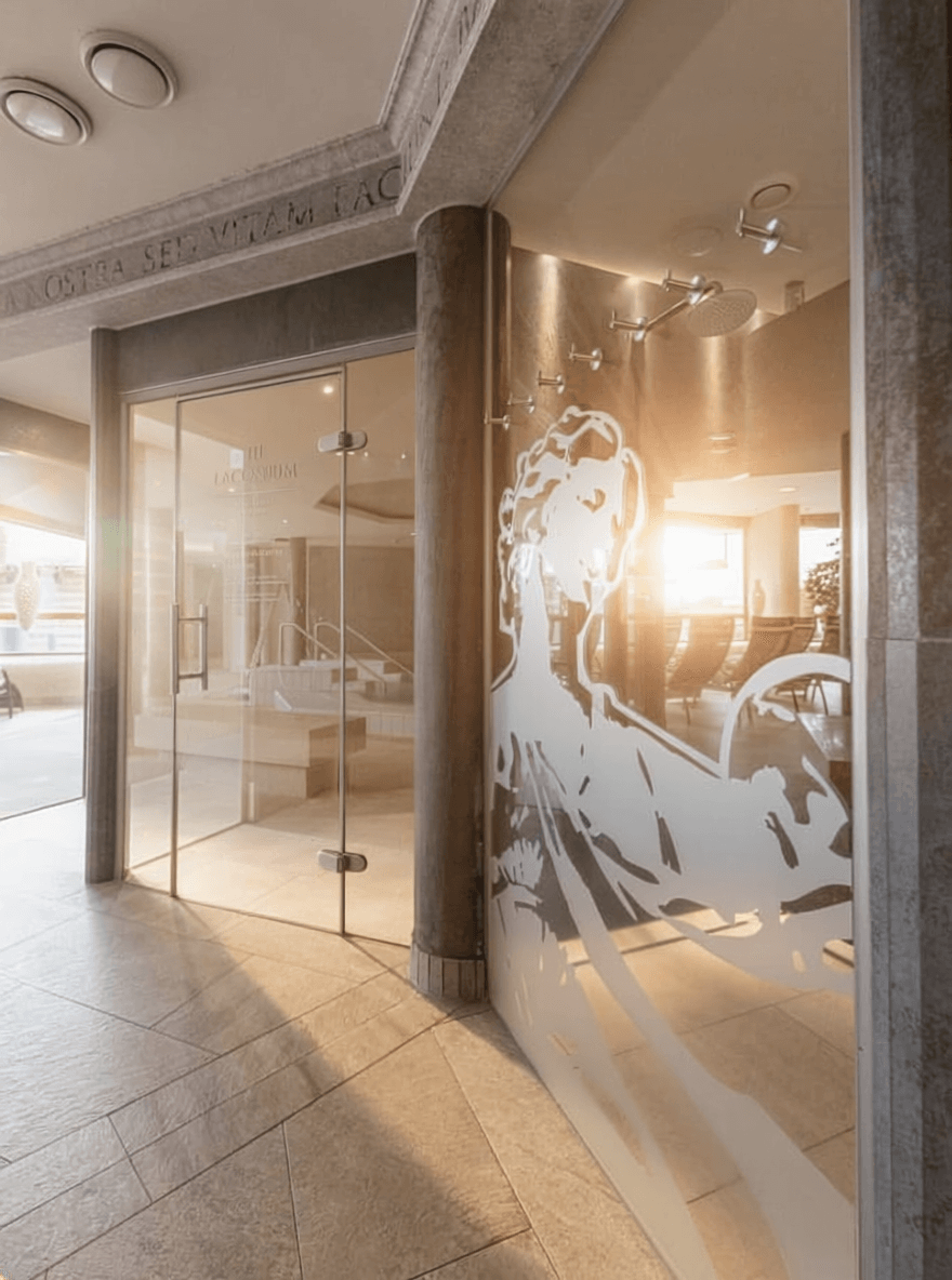Entrance area with a glass wall featuring a stylized figure and a column in a warmly lit interior