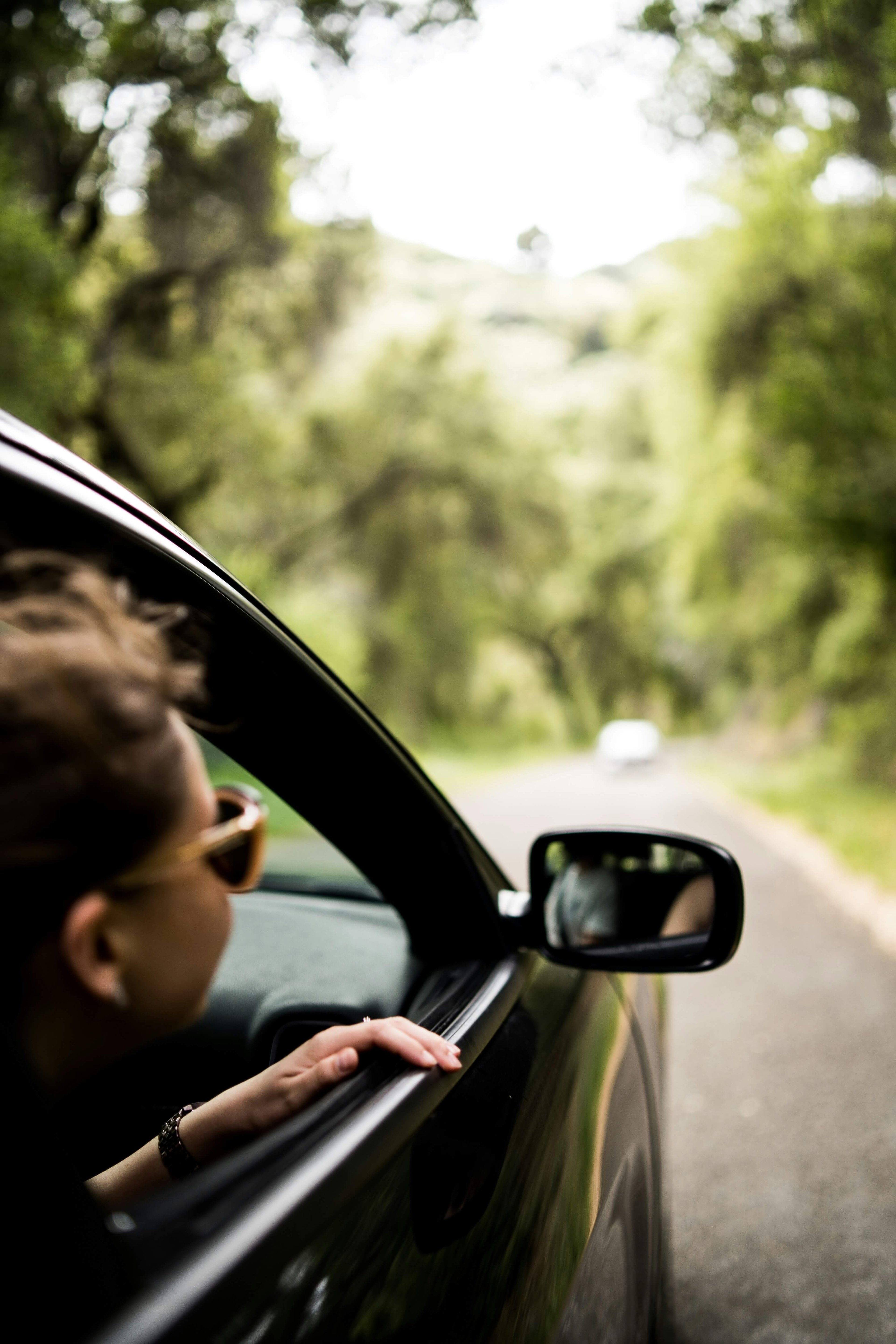 Woman sits in the car and looks out of the passenger window into the green surroundings.
