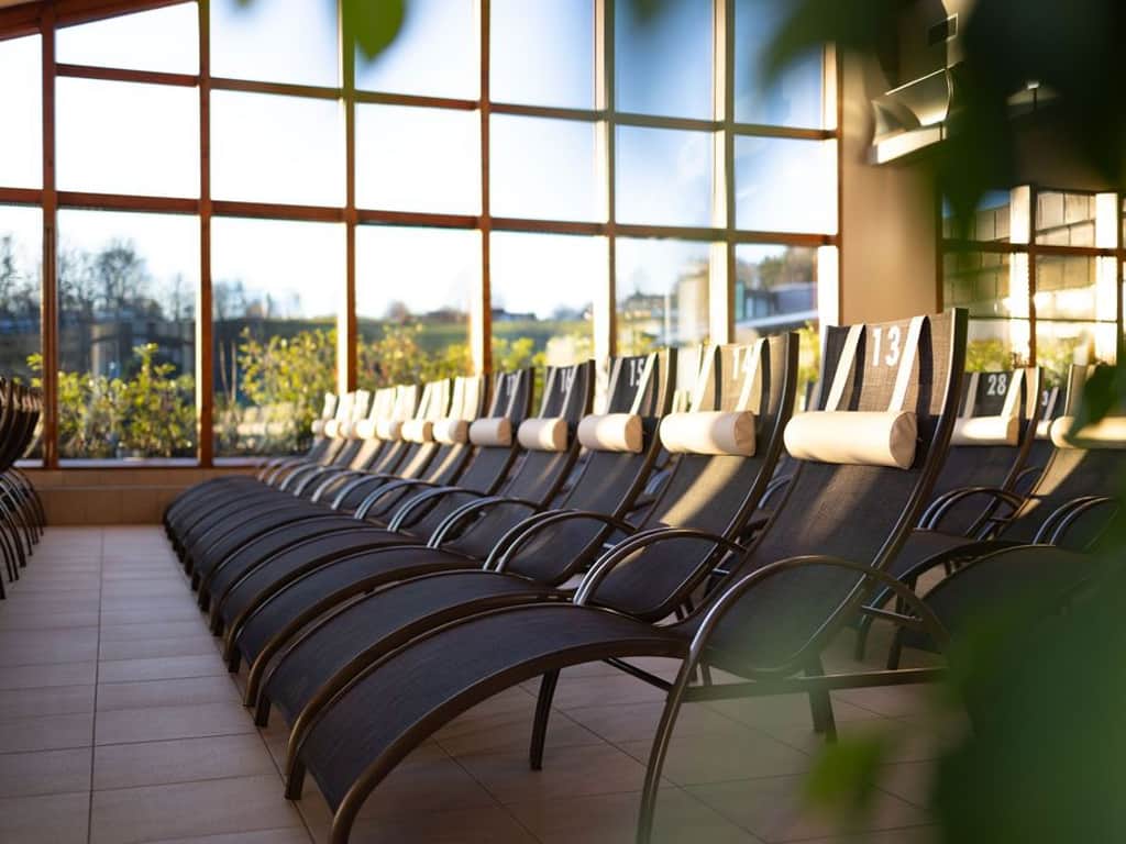 Ansicht mehrerer schwarze Liegen im Thermenbad. Im Hintergrund Fensterfront mit Ausblick in die Region.