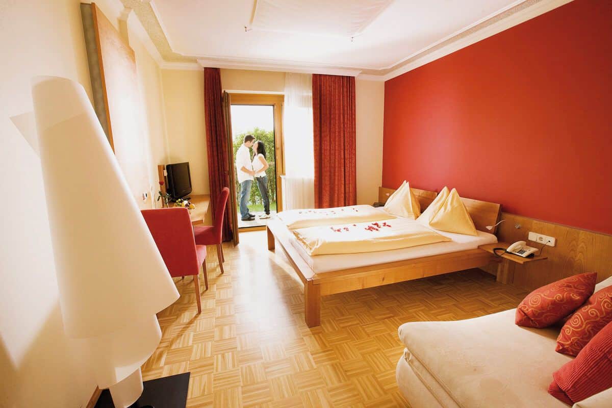 Ein Doppelzimmer im Panoramahof mit Balkon, am Balkon küsst sich ein Paar.