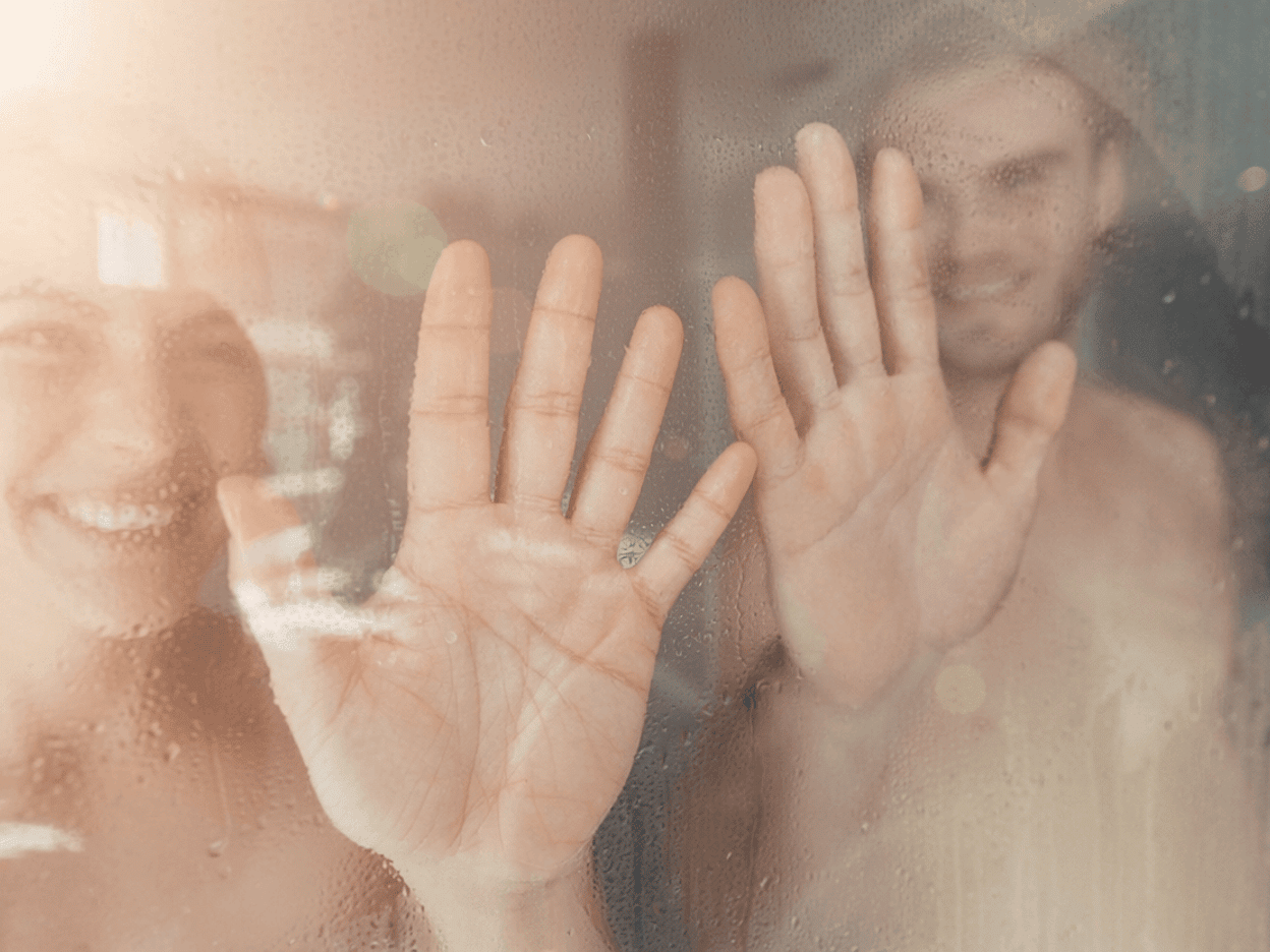 Ein Paar hält die Hände an die Glasscheibe des Dampfbades.