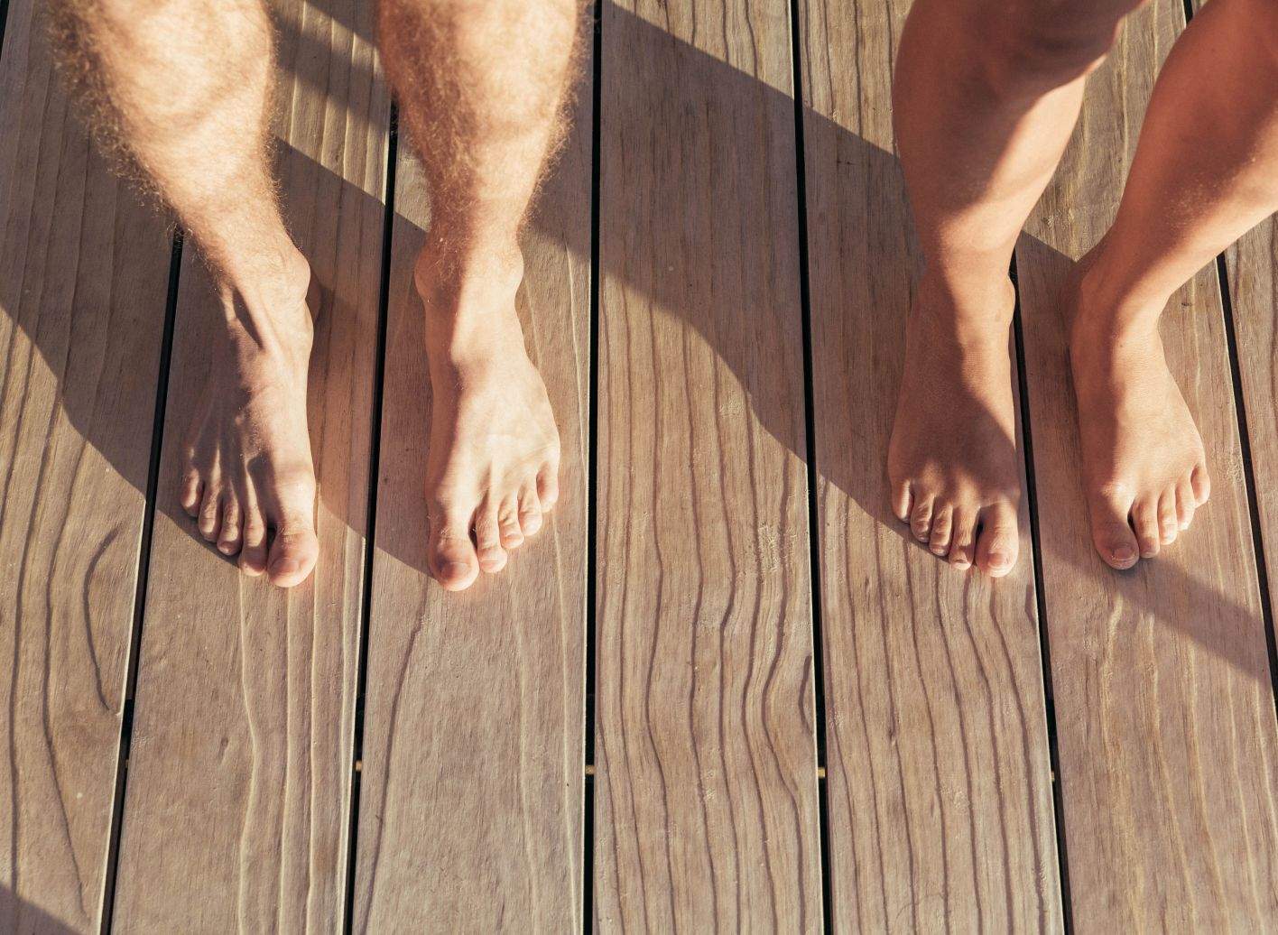 Two pairs of bare legs on the wooden floor of the naturist area.