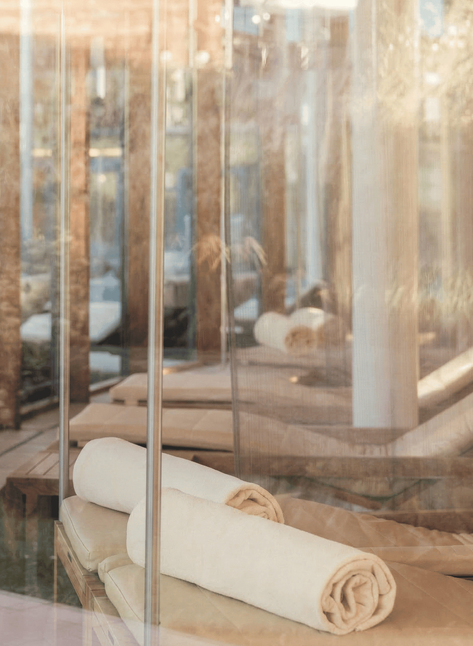 Zwei zusammengerollte Handtücher liegen auf einer Liege in einem Pavillon mit Glaswänden