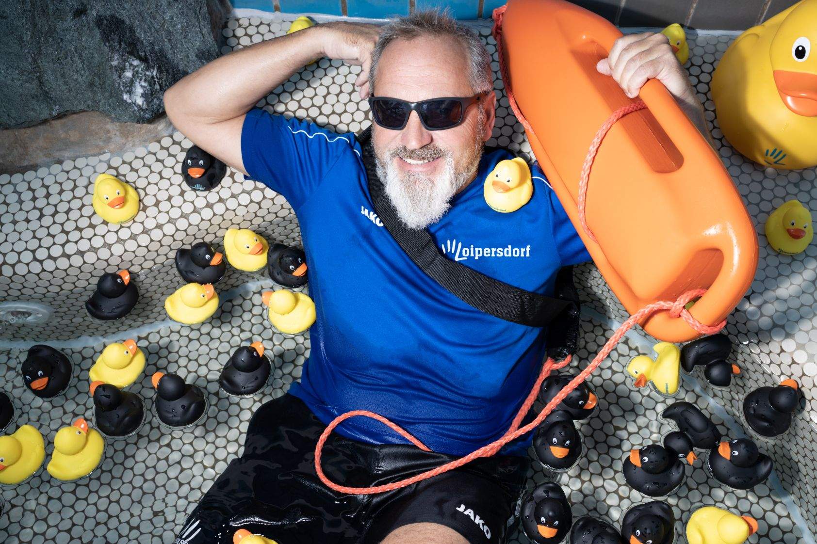 Ein Bademeister grinst und planscht mit Gummienten.