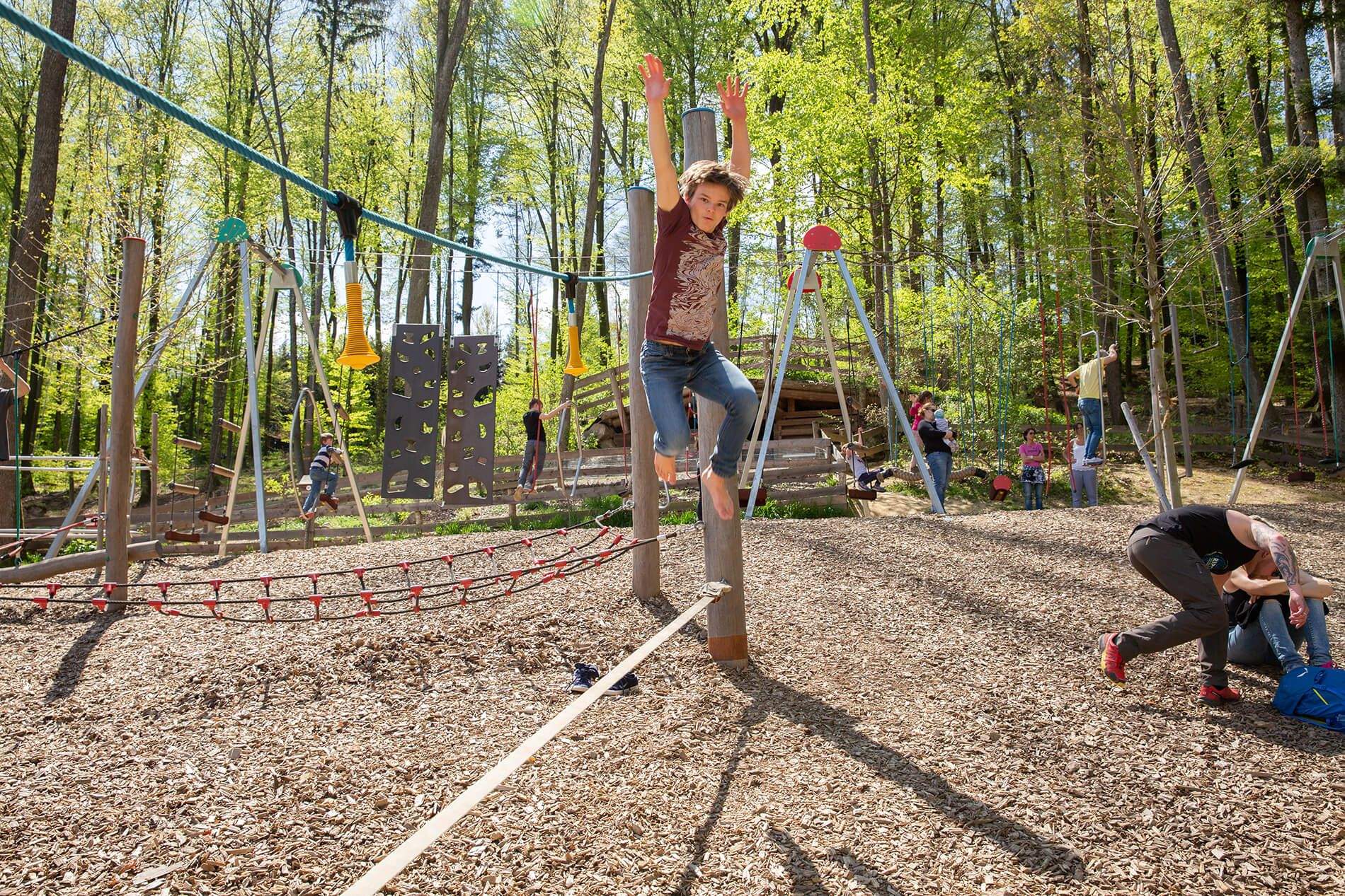 A boy climbs over a net in the forest playground.