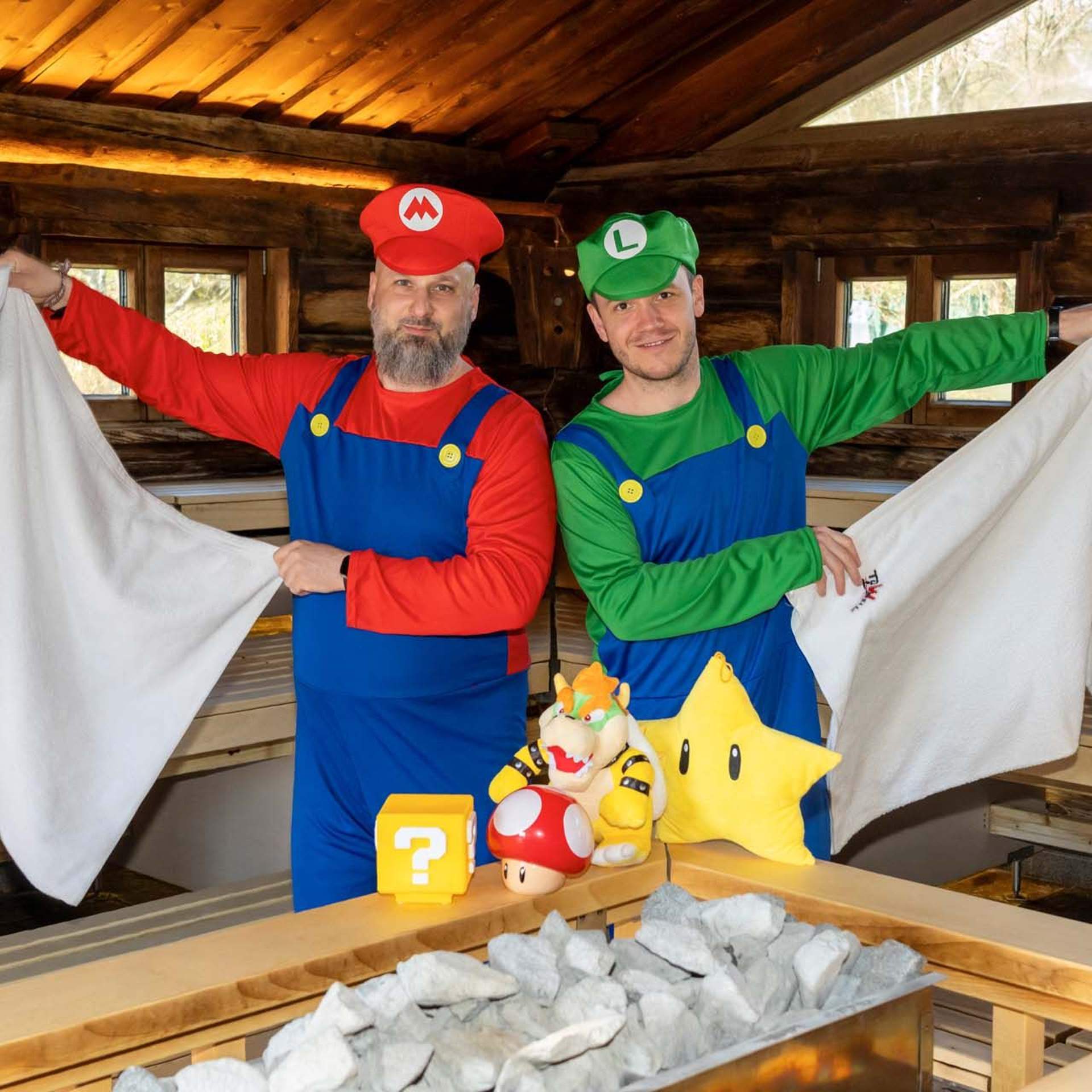 Two sauna masters during the show infusion in the panorama sauna in the Schaffelbad. The sauna masters wear a Supermario costume. 