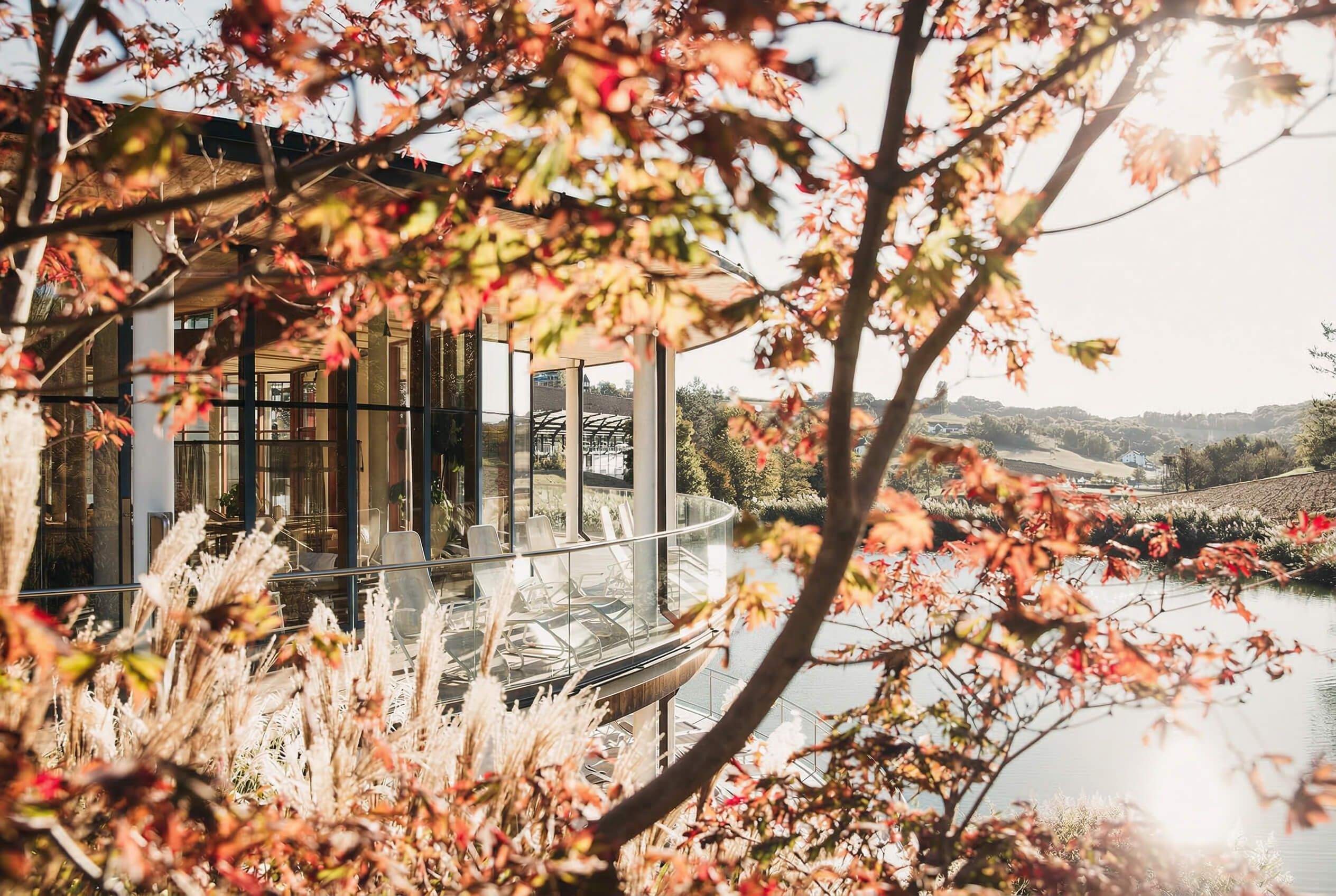 Moderner Pavillon mit Glasfronten in herbstlicher Landschaft mit See und Hügeln