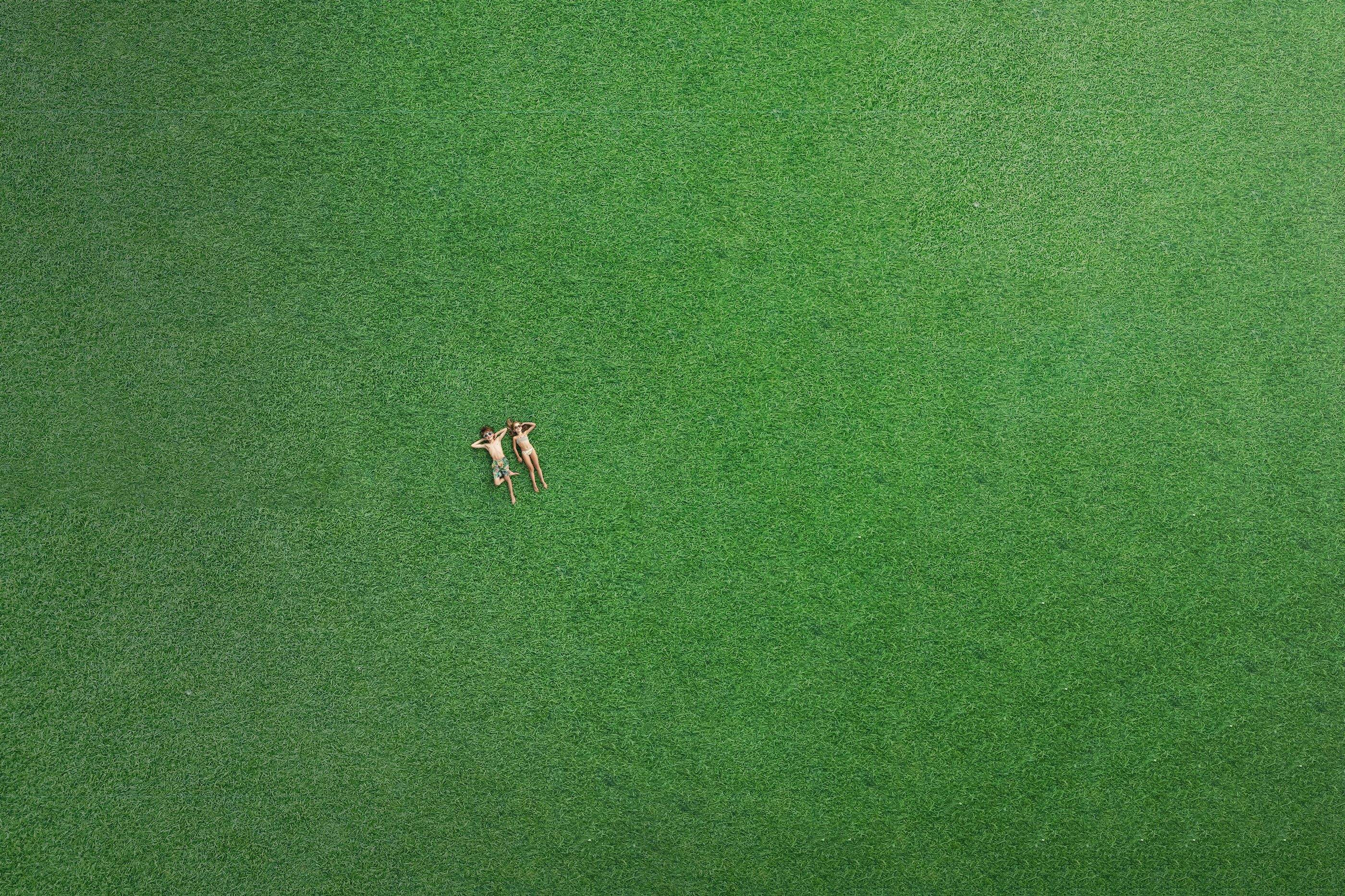 Rießige grüne Liegefläche im Freibereich und zwei Kinder die inder Wiese liegen. 