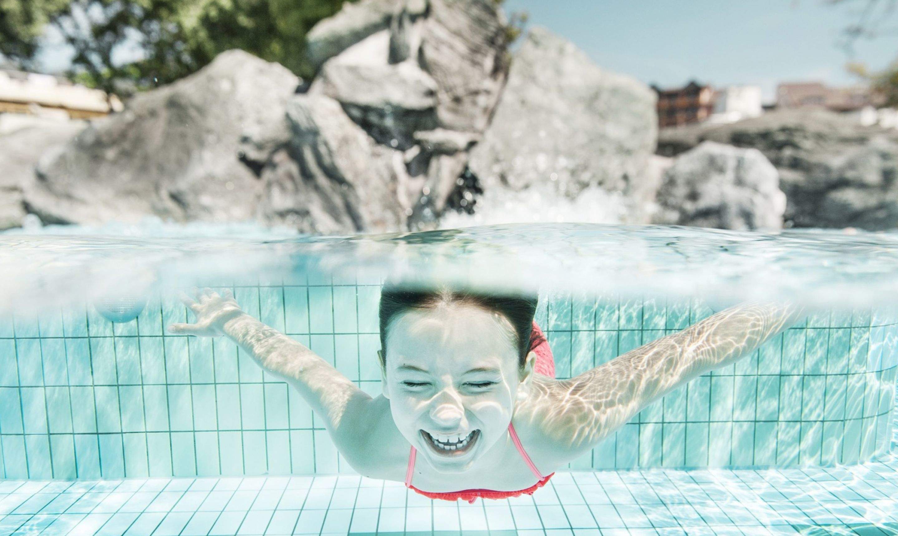 Ein Kind taucht im Außenbecken der Therme Loipersdorf und lacht.