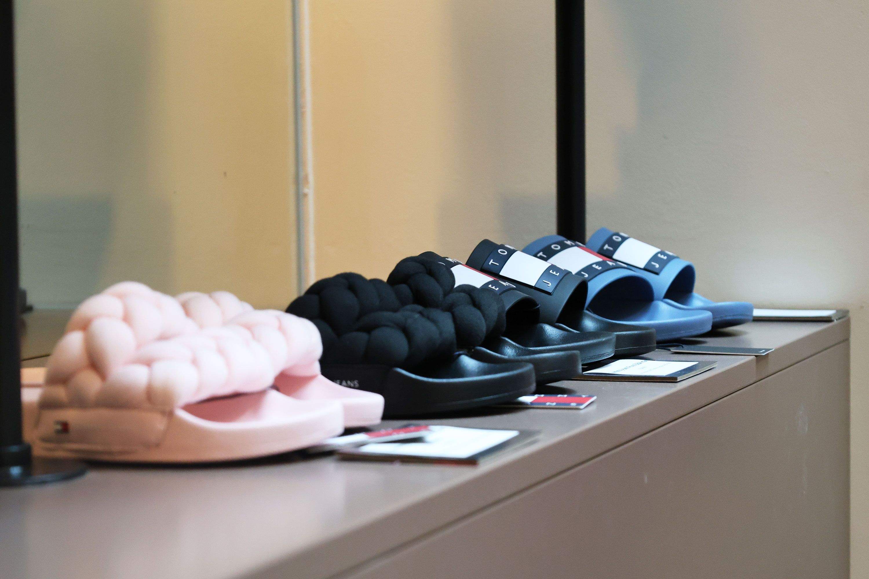 Vier Paar Hausschuhe in Pastellrosa, Schwarz und Blau mit gepolsterten, knotenartigen Riemen auf einer Ablage.