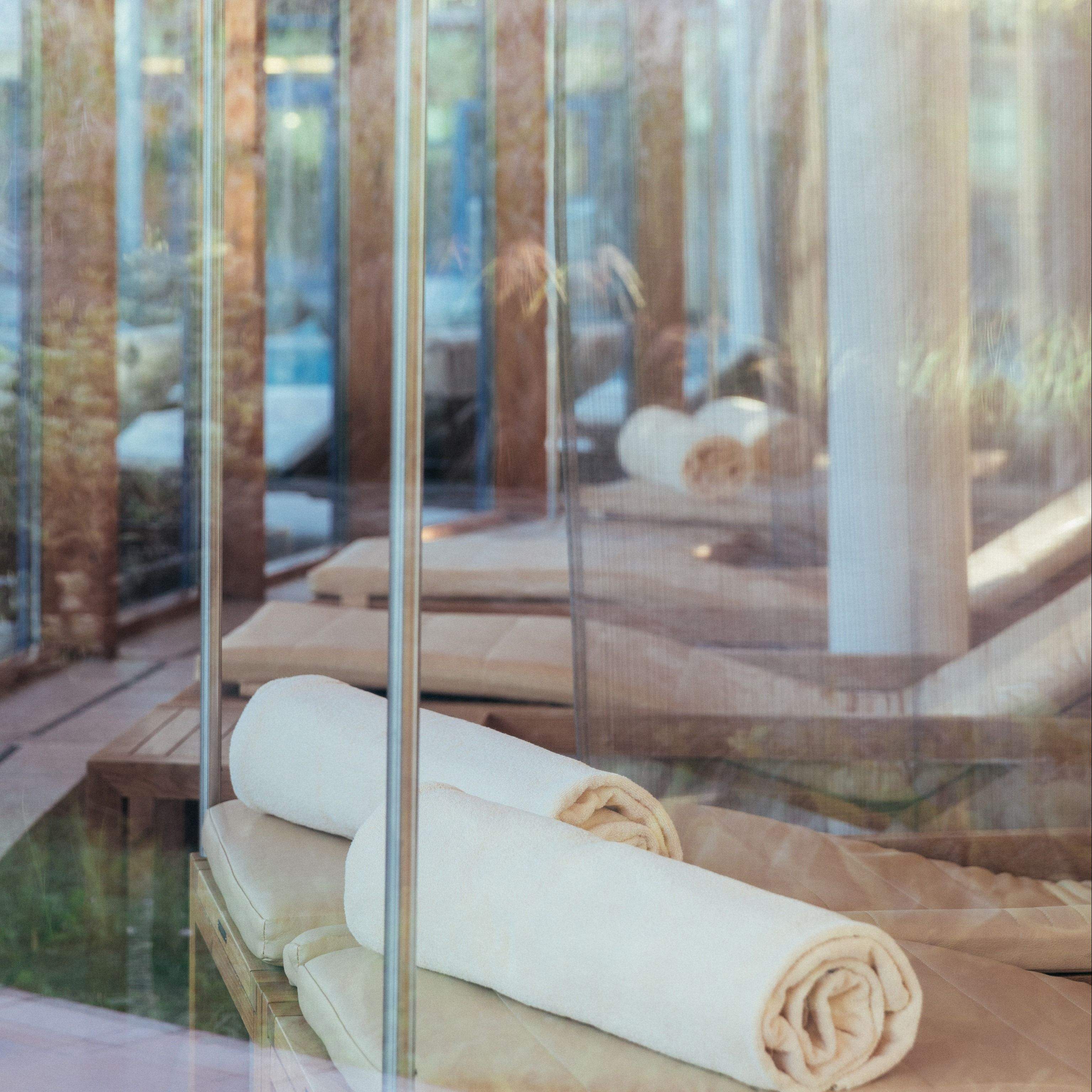 Aufgerollte weiße Handtücher auf einer Liege im Schaffelbad Seepavillon mit Glaswänden
