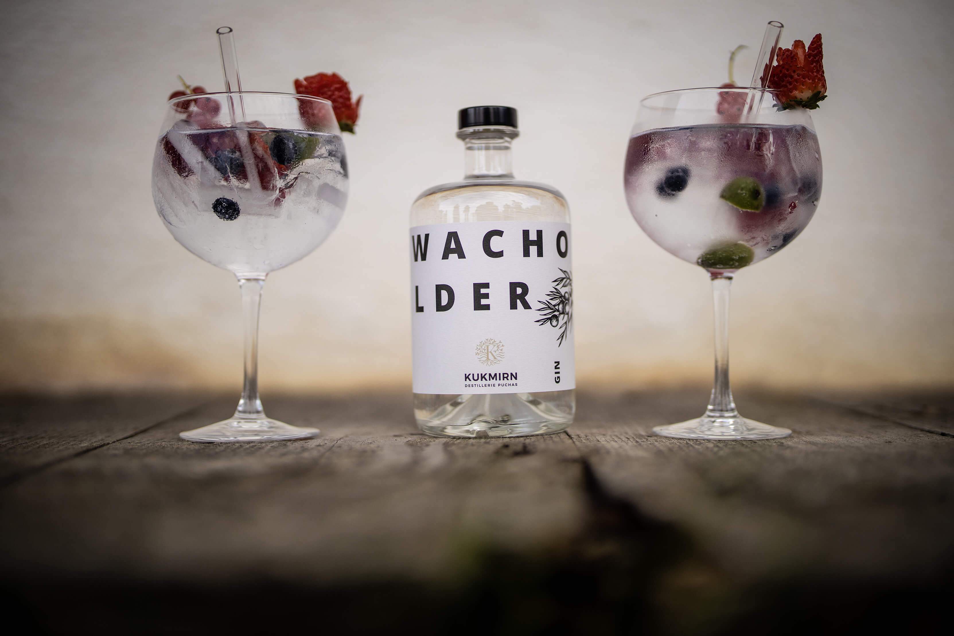 Eine Flasche Wacholdergin mit zwei Gläsern Gin Tonic angerichtet.