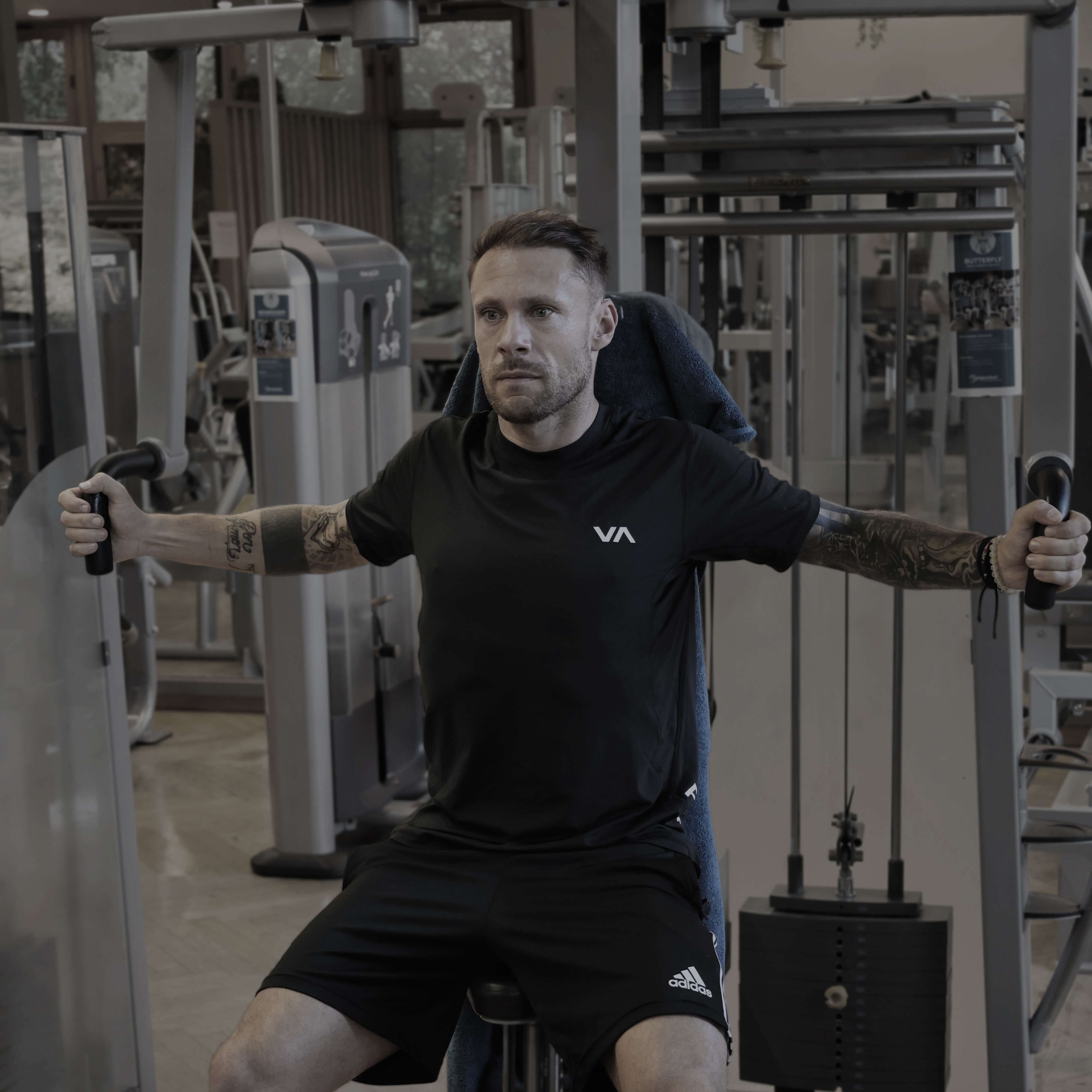 Mann sitzt an Fitnessgerät und führt Butterfly-Übung mit ausgestreckten Armen aus