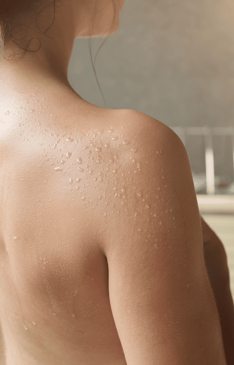 Nackter Rücken und Schulter einer Person mit Wassertropfen auf der Haut vor unscharfem Hintergrund
